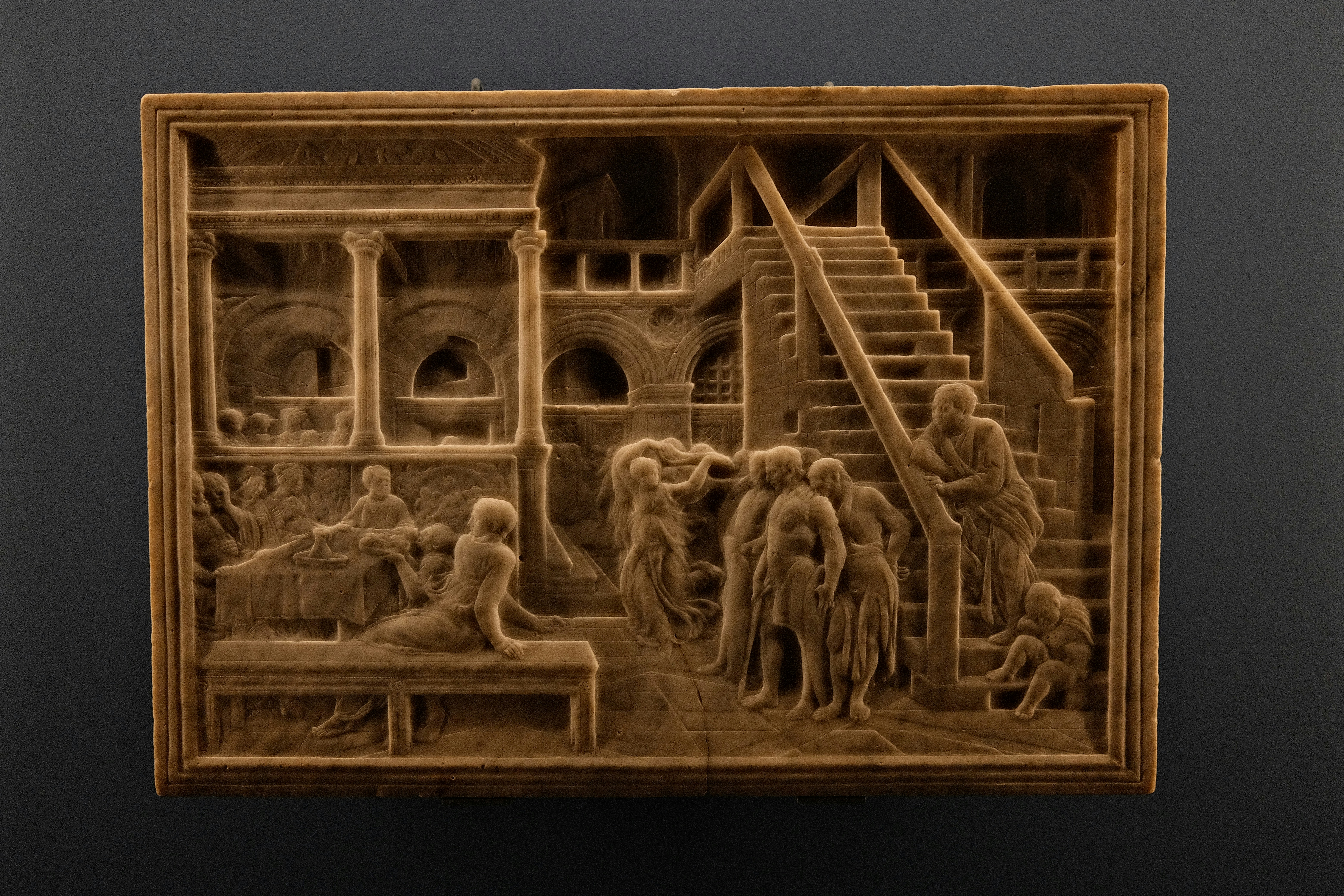 A stone relief carving of people in an architectural setting with stairs and columns