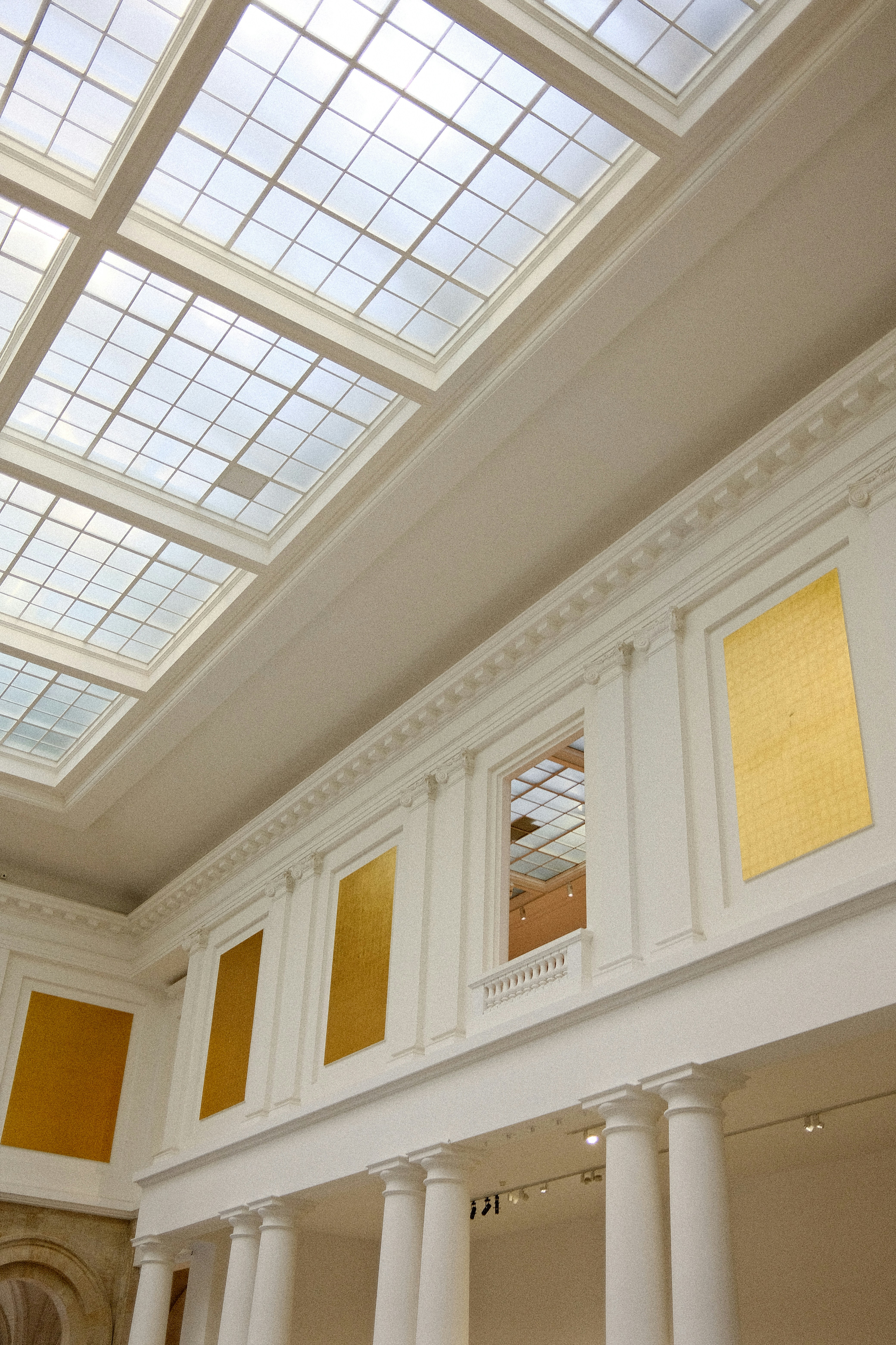 White walls with gold panels and a grid skylight in a museum gallery