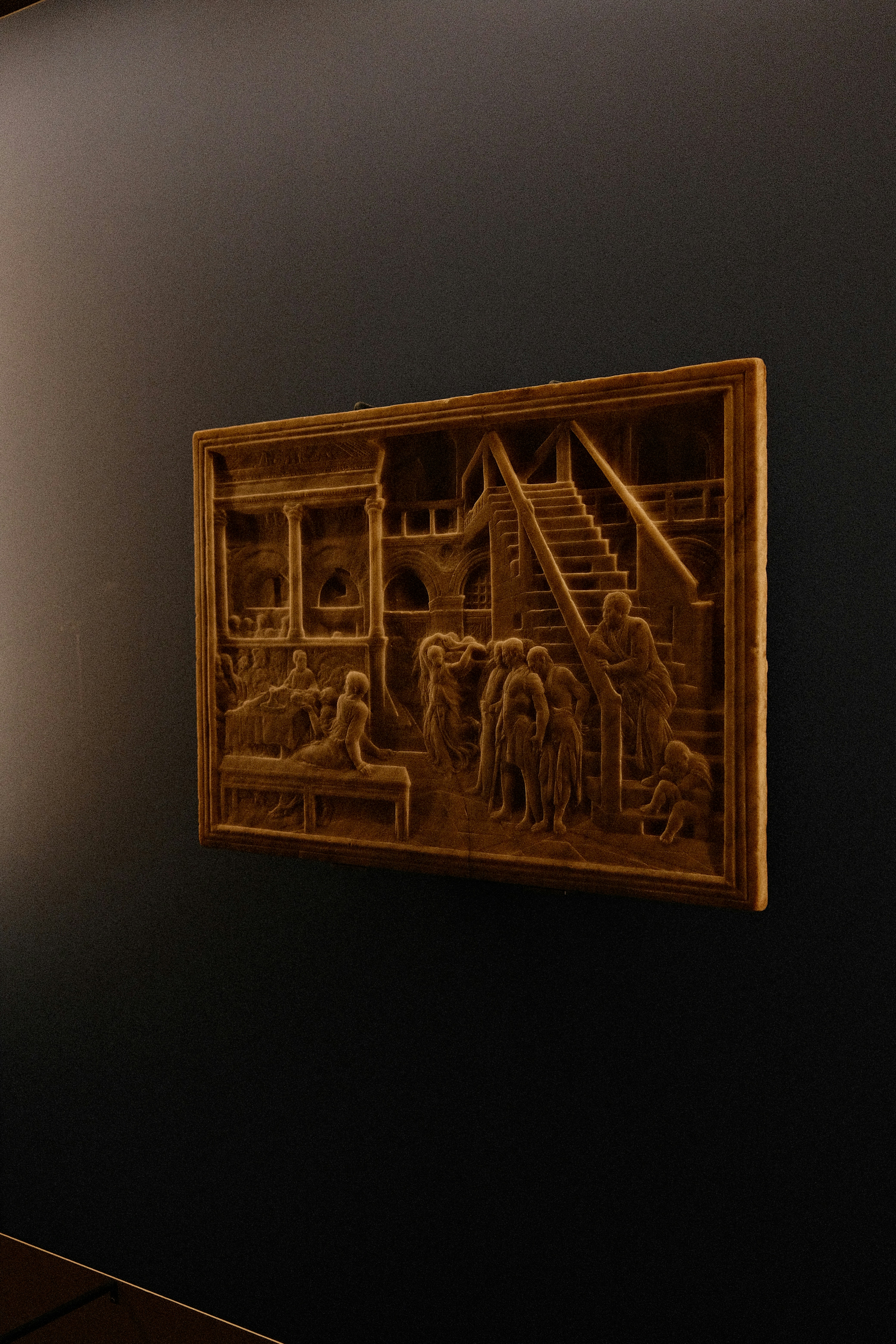 A stone relief depicting people in an architectural setting on a dark wall