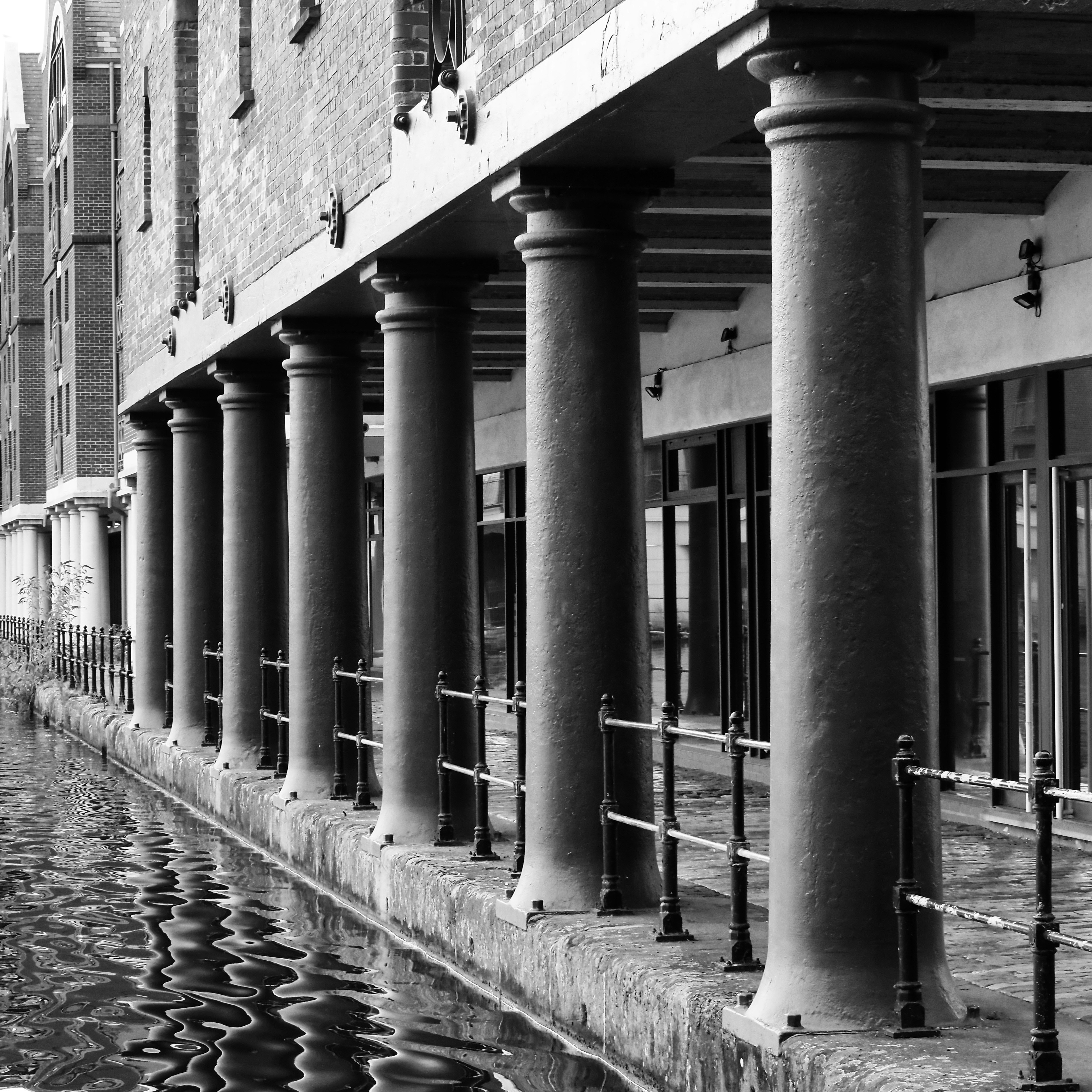 Black and white view of brick building columns along a canal walkway