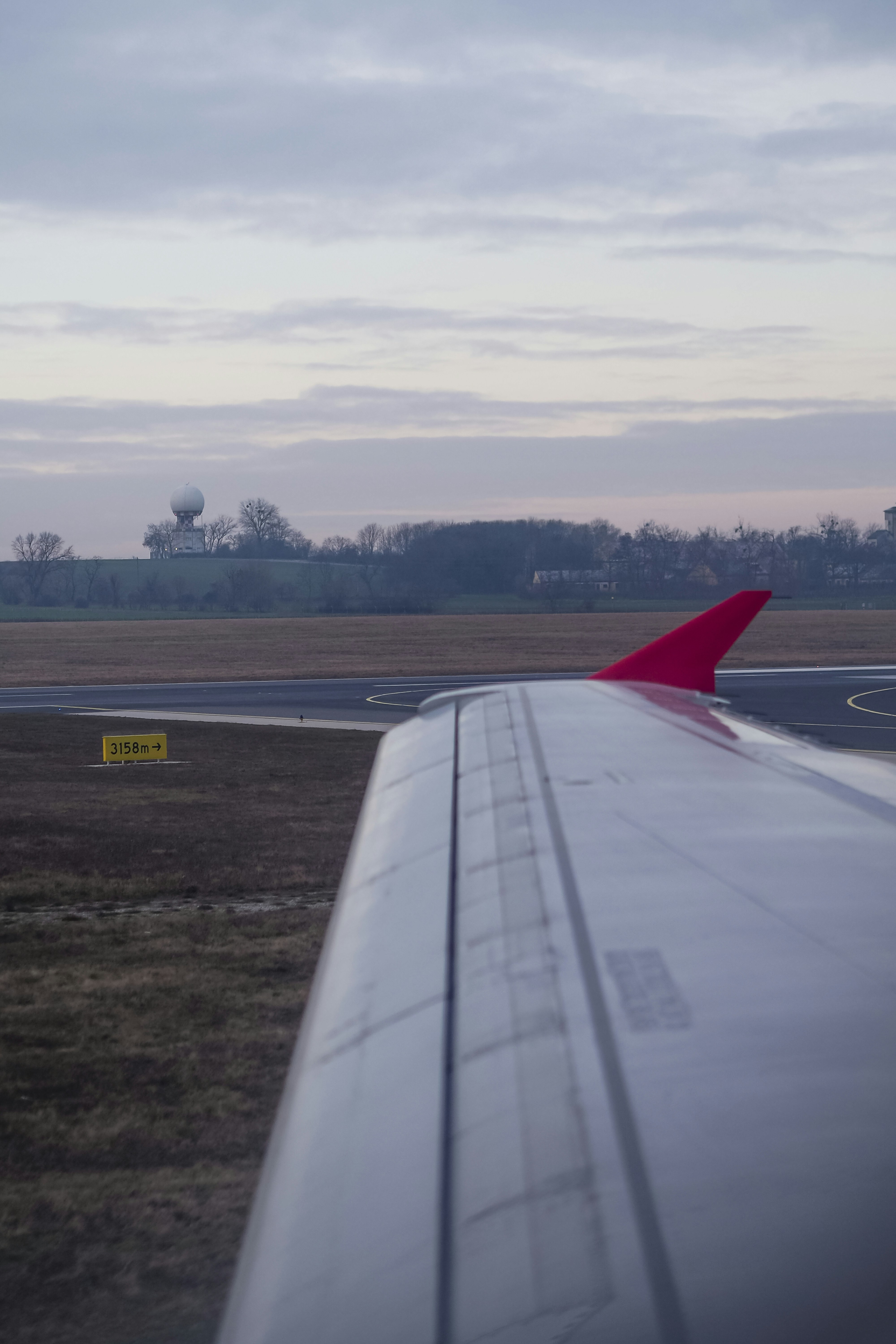 Airplane wing with a red winglet over an airport runway at low light