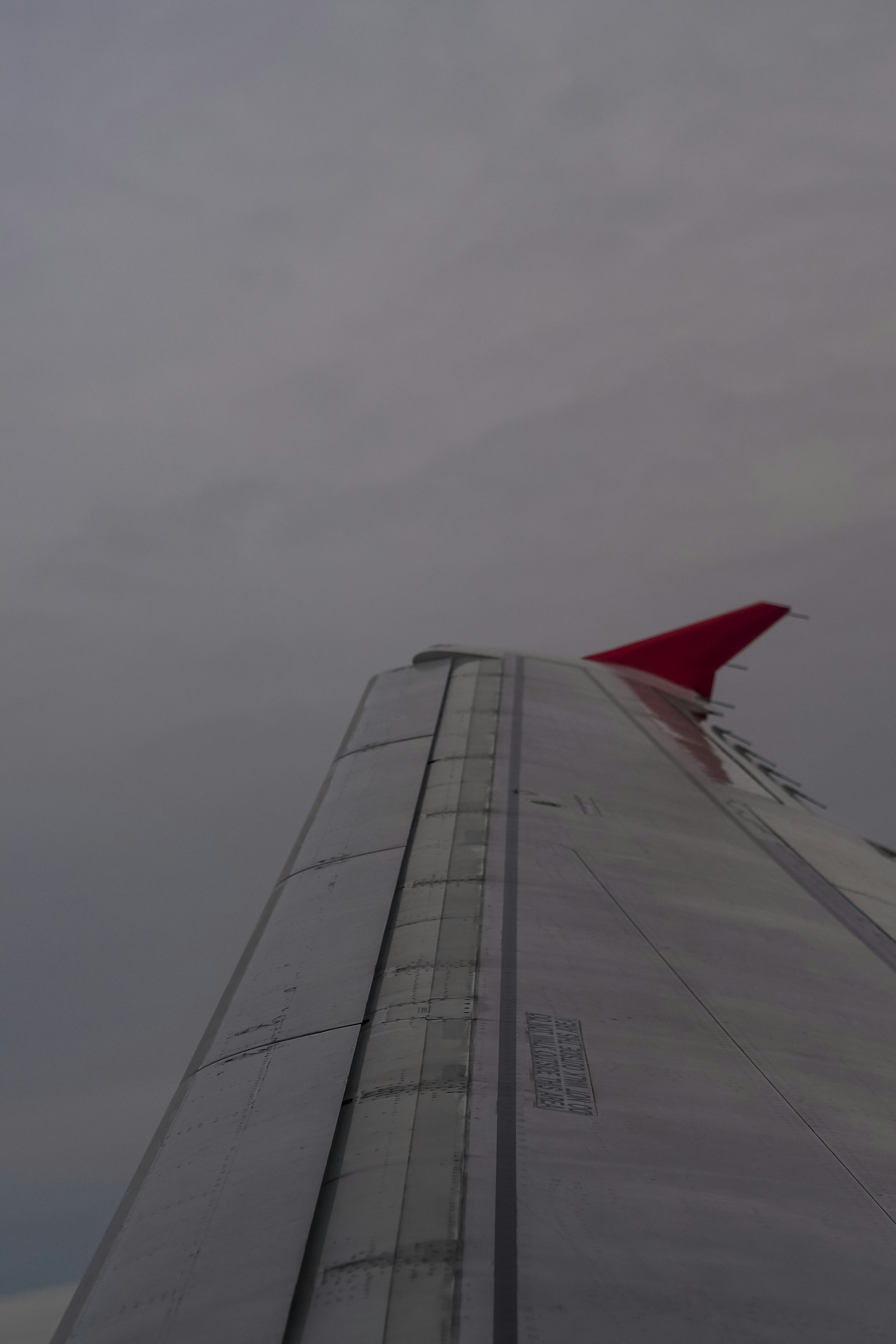 An airplane wing with a red winglet against a grey overcast sky