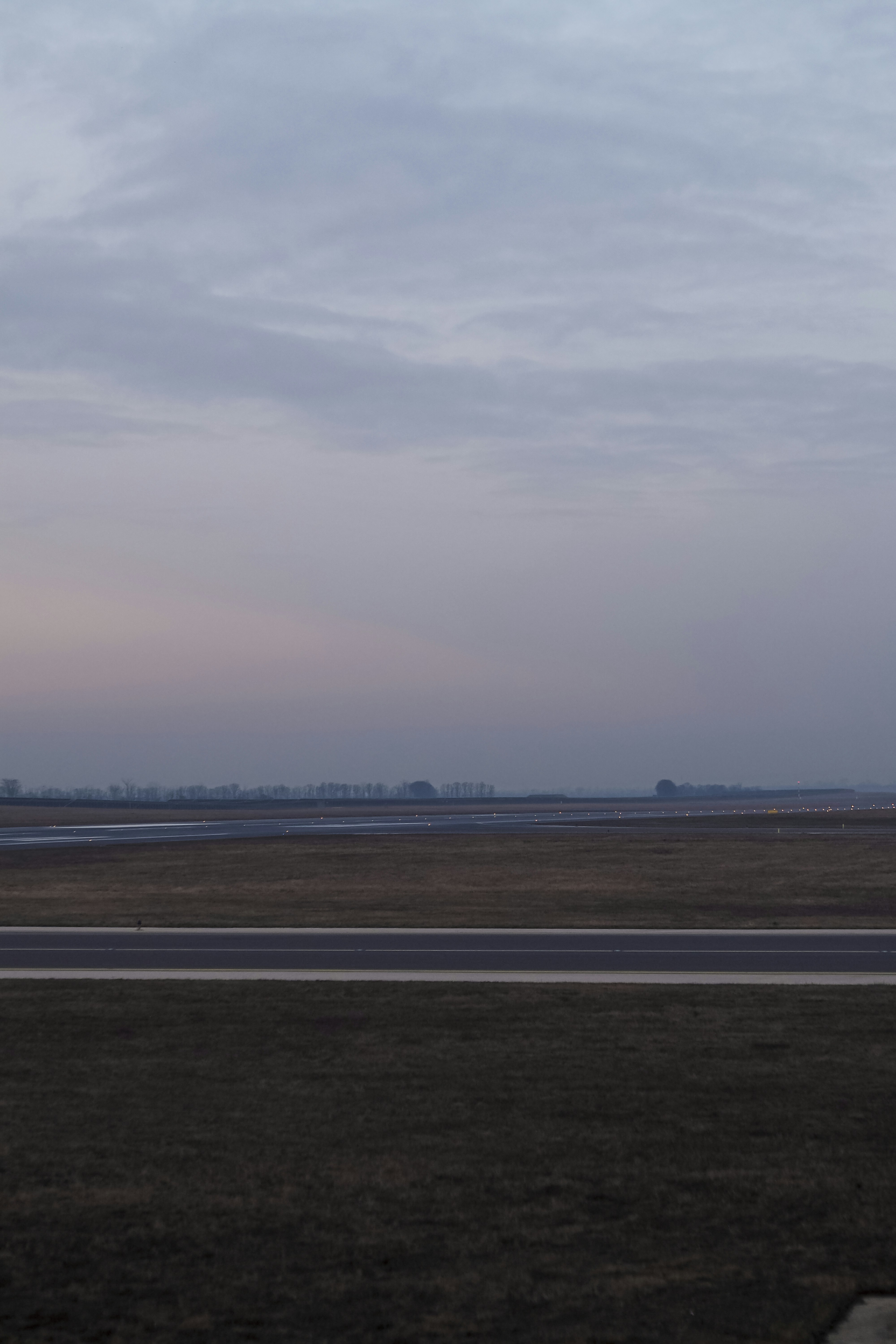 An airport runway with small lights under a soft grey and pink sky