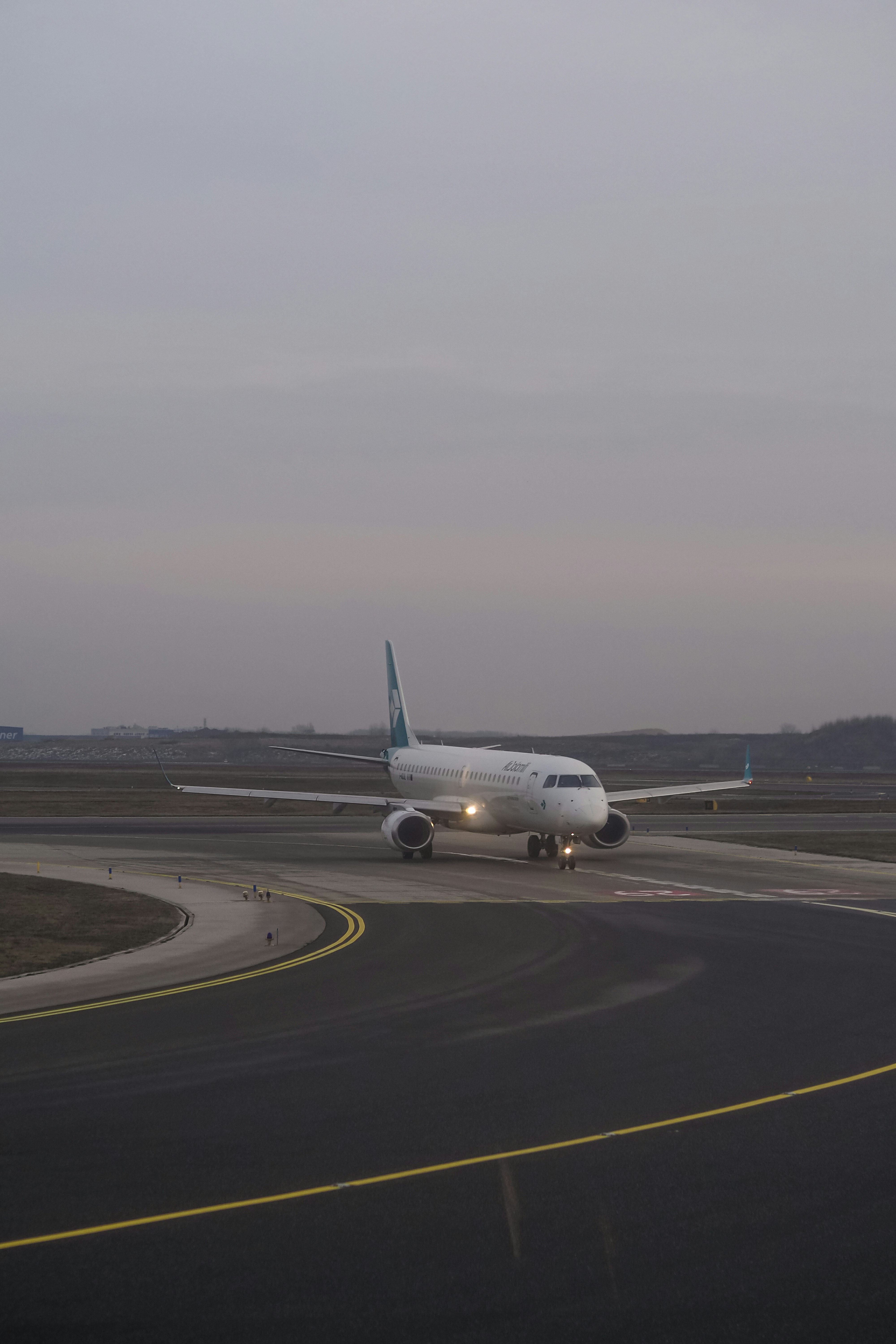 A white passenger airplane taxiing on an airport runway under a grey sky