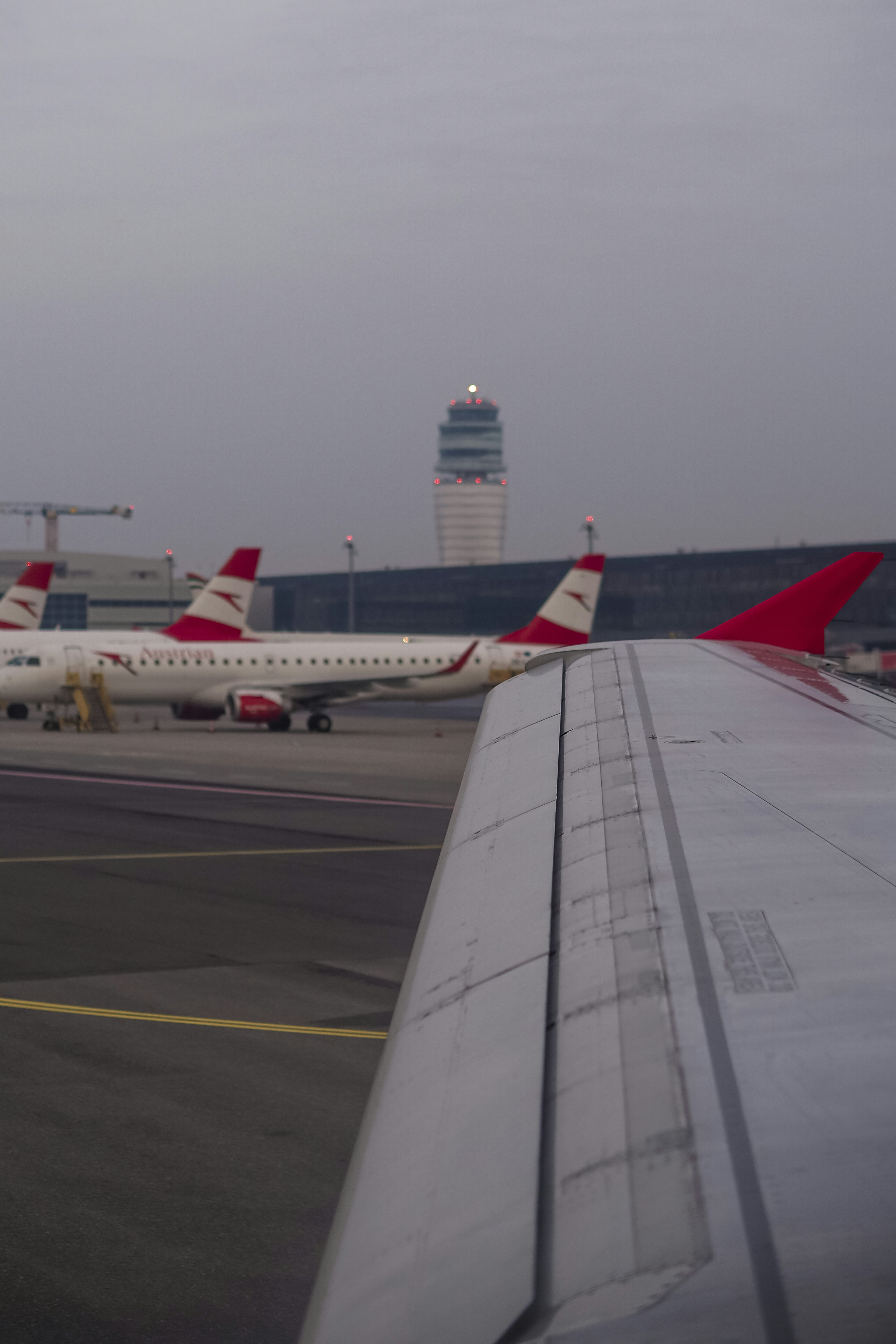 An airplane wing in the foreground with parked aircraft and a control tower