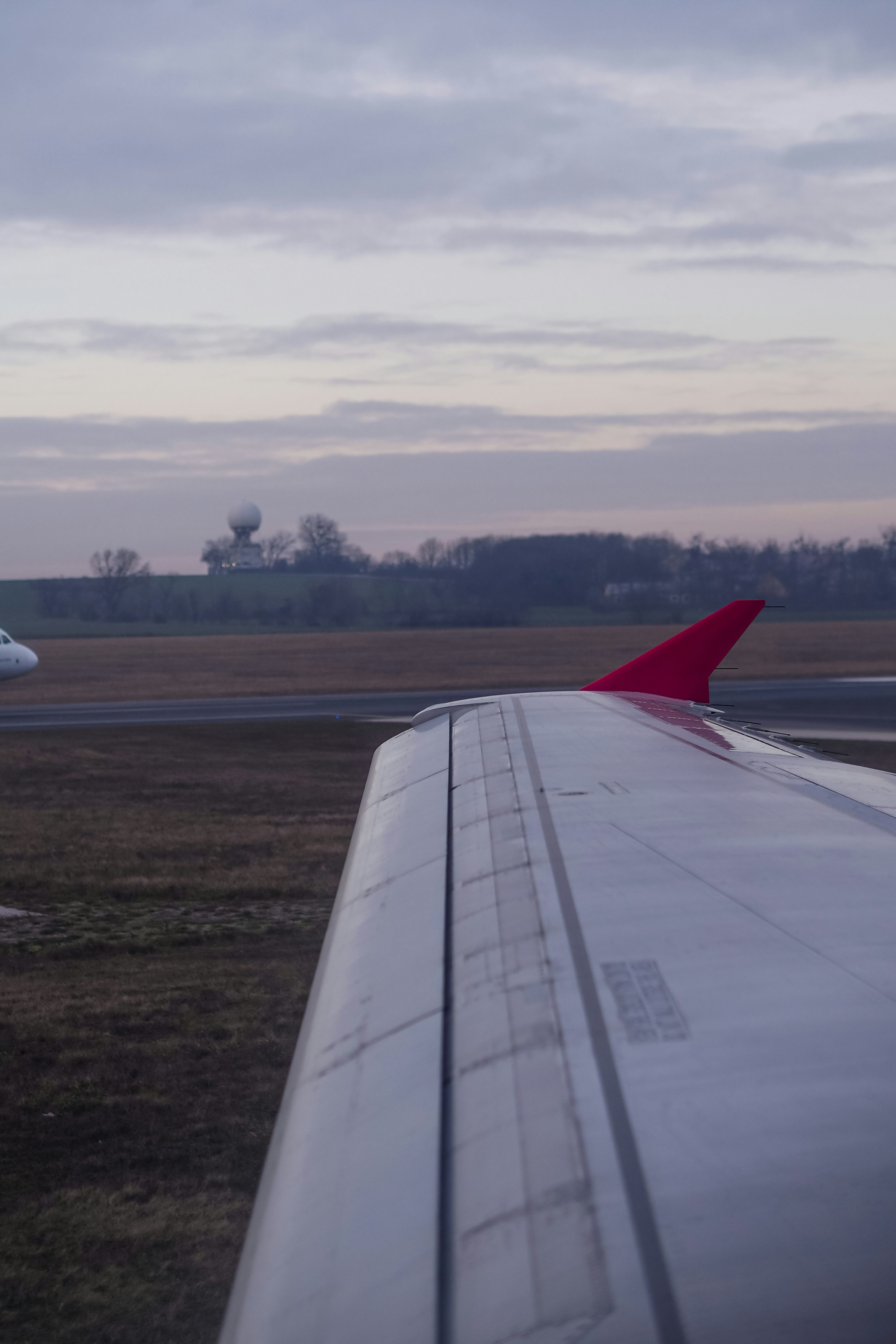 An airplane wing with a red winglet above a grassy airfield at dusk