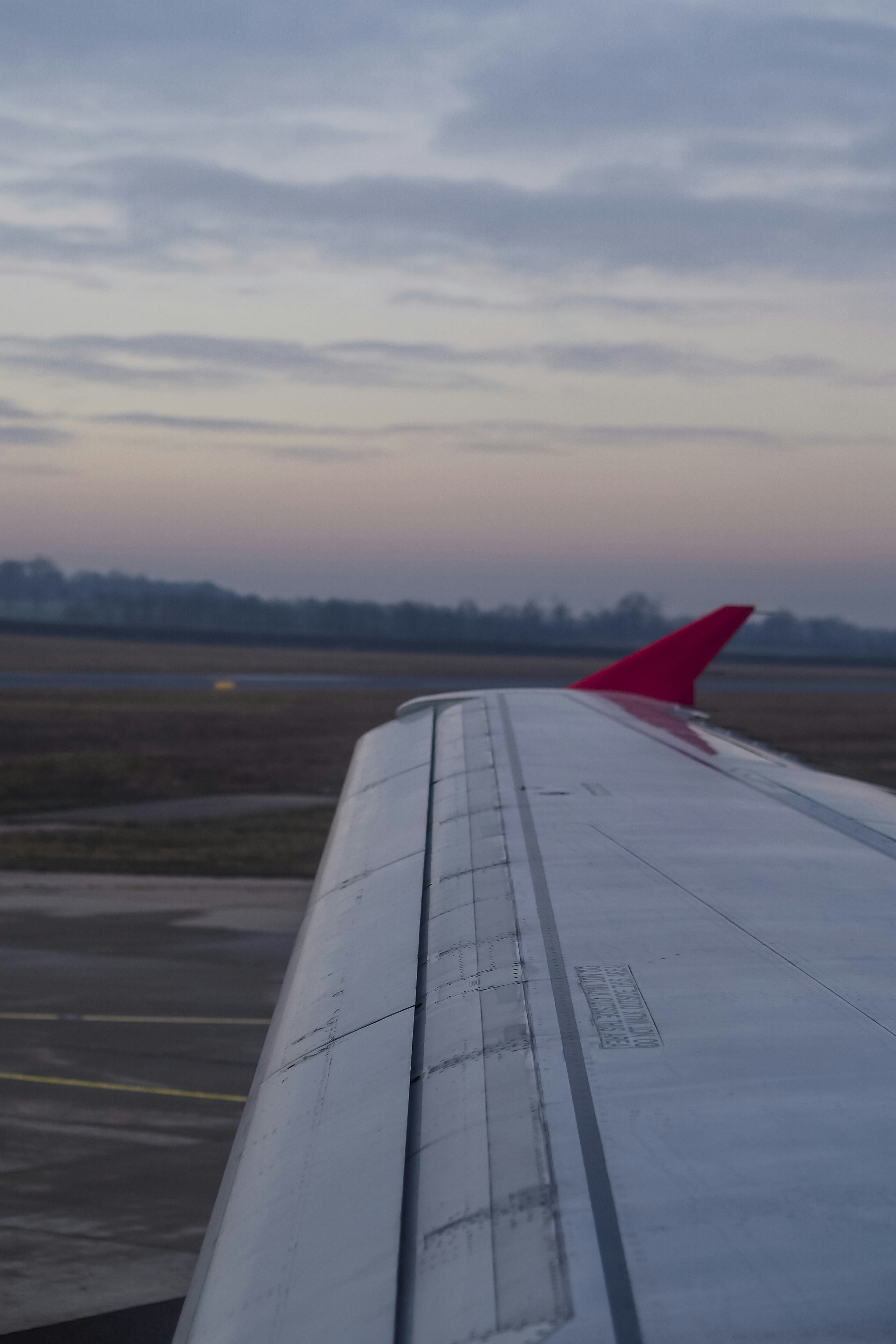 An airplane wing with a red winglet above an airport runway at low light