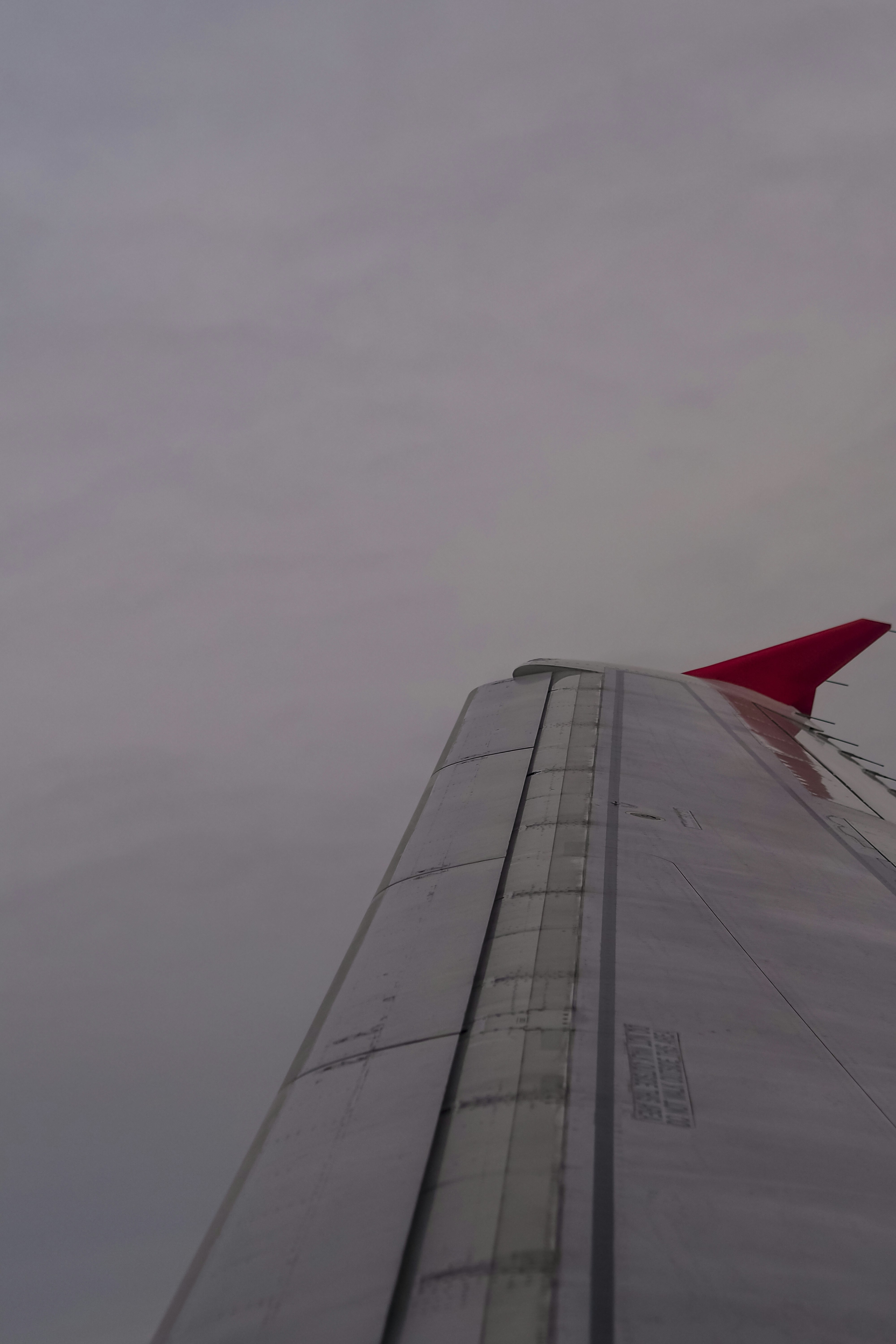An airplane wing with a red winglet against a cloudy grey sky