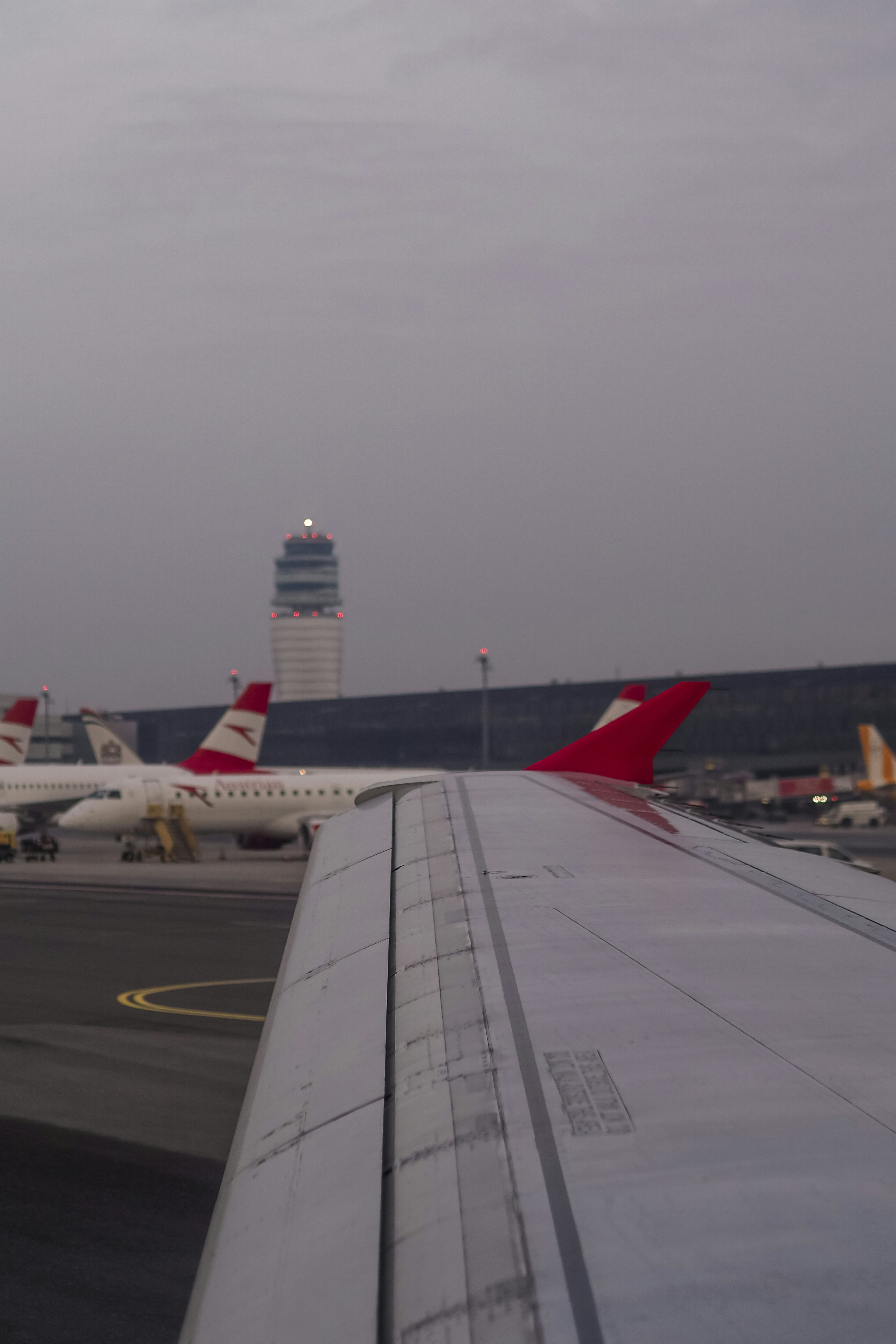An airplane wing in the foreground with an airport control tower in the distance