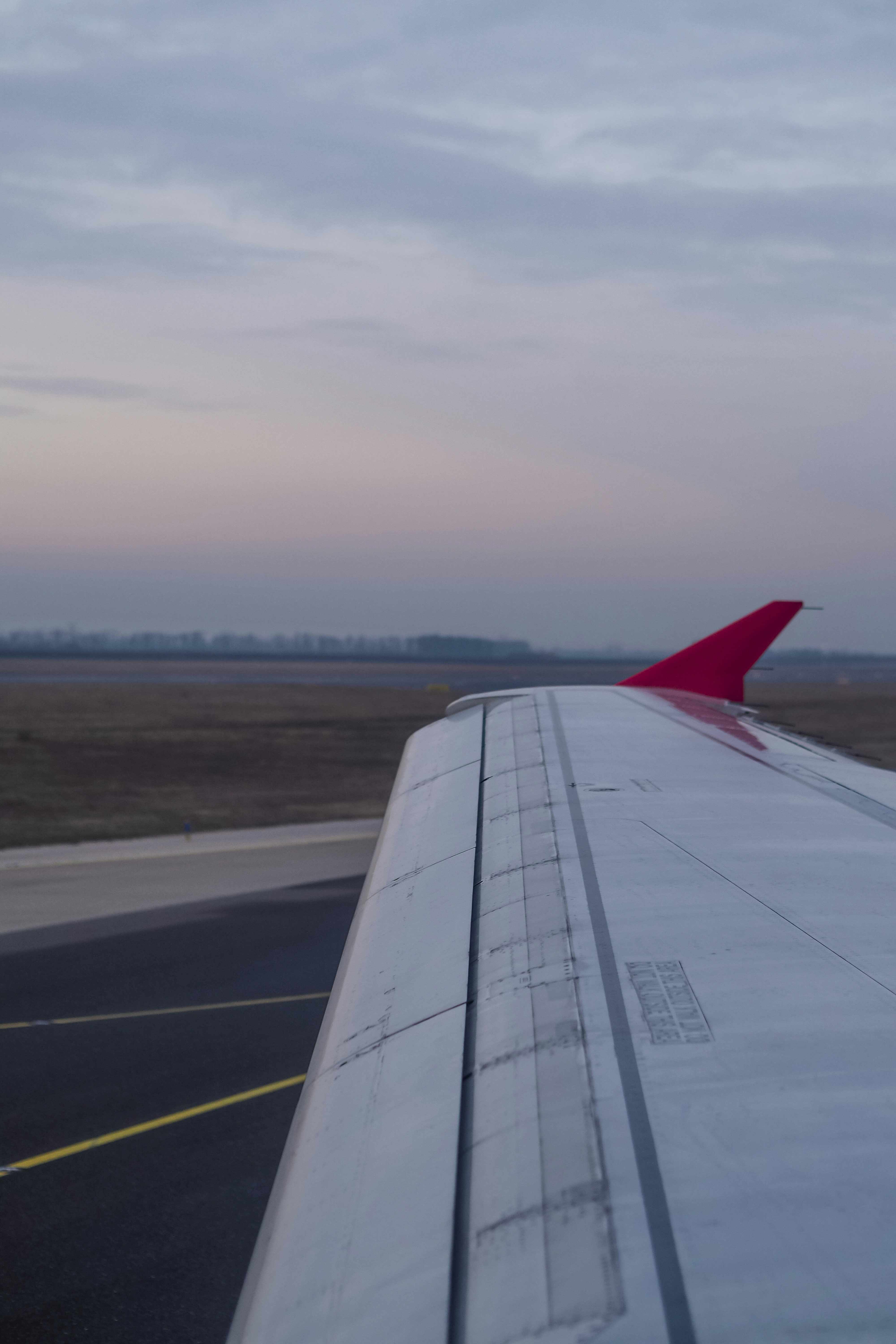 Airplane wing with a red winglet above an airport runway at dusk