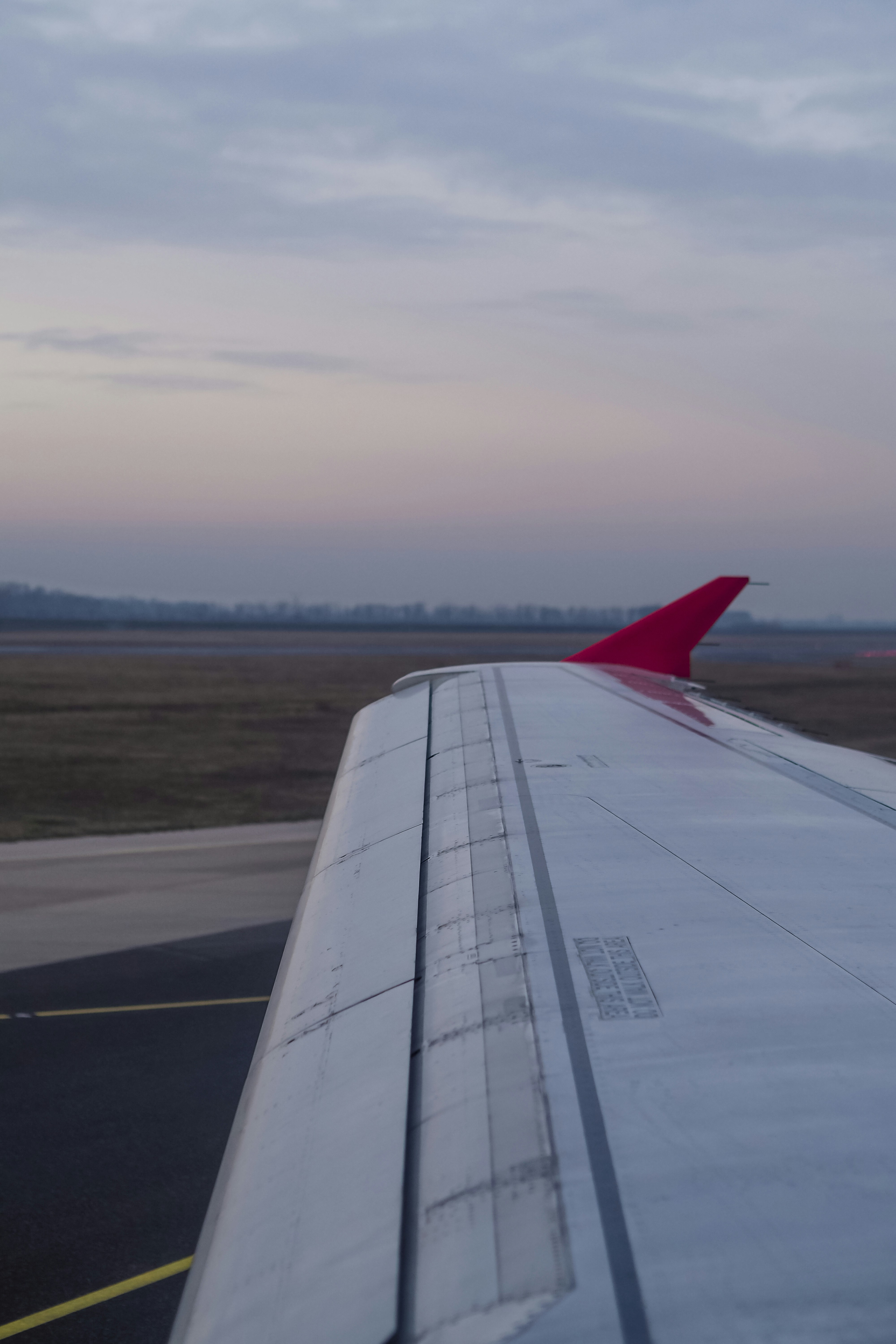 An airplane wing with a red winglet above an airport runway at dusk