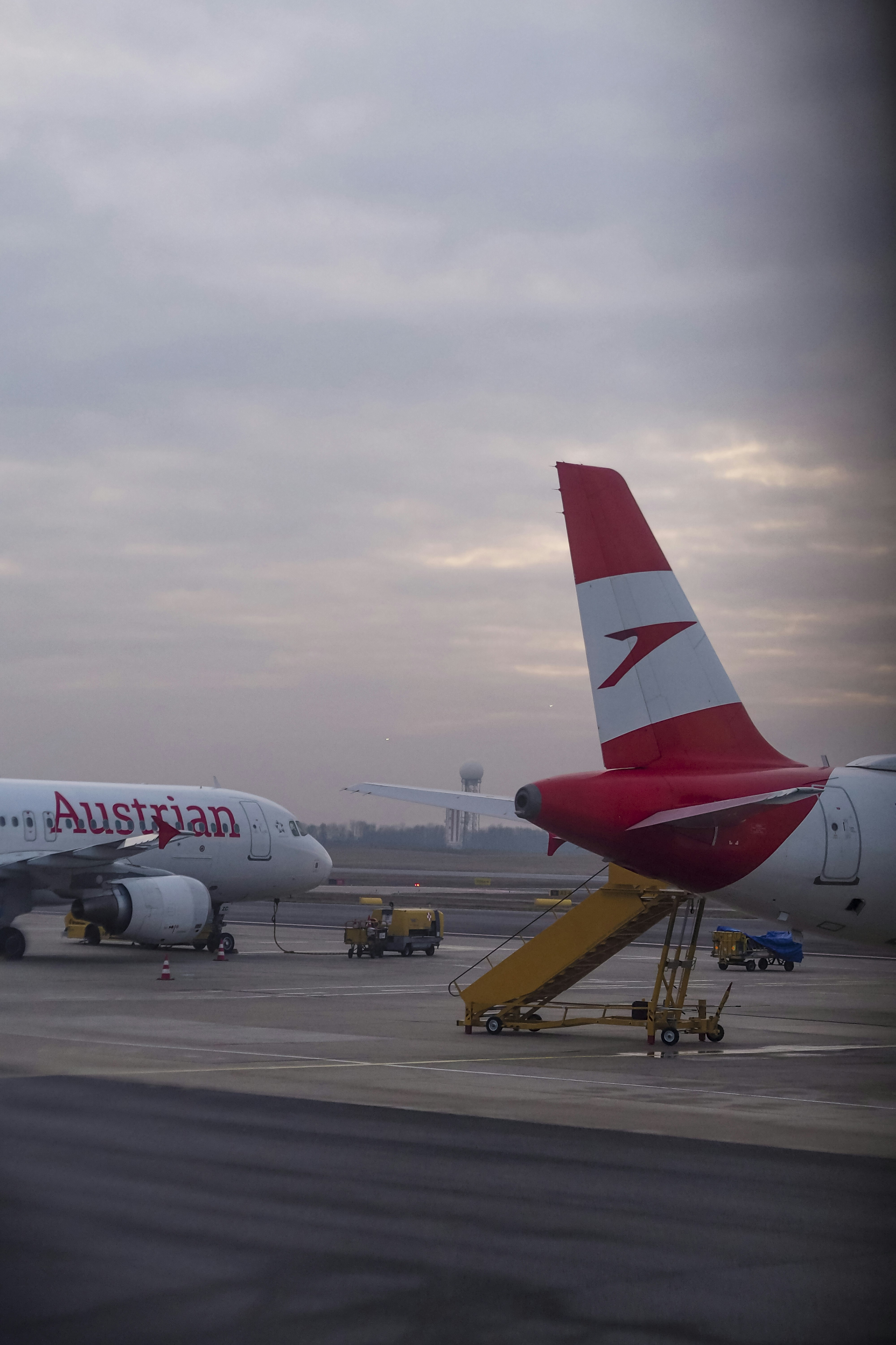 Two Austrian Airlines planes parked on an airport tarmac under a cloudy sky