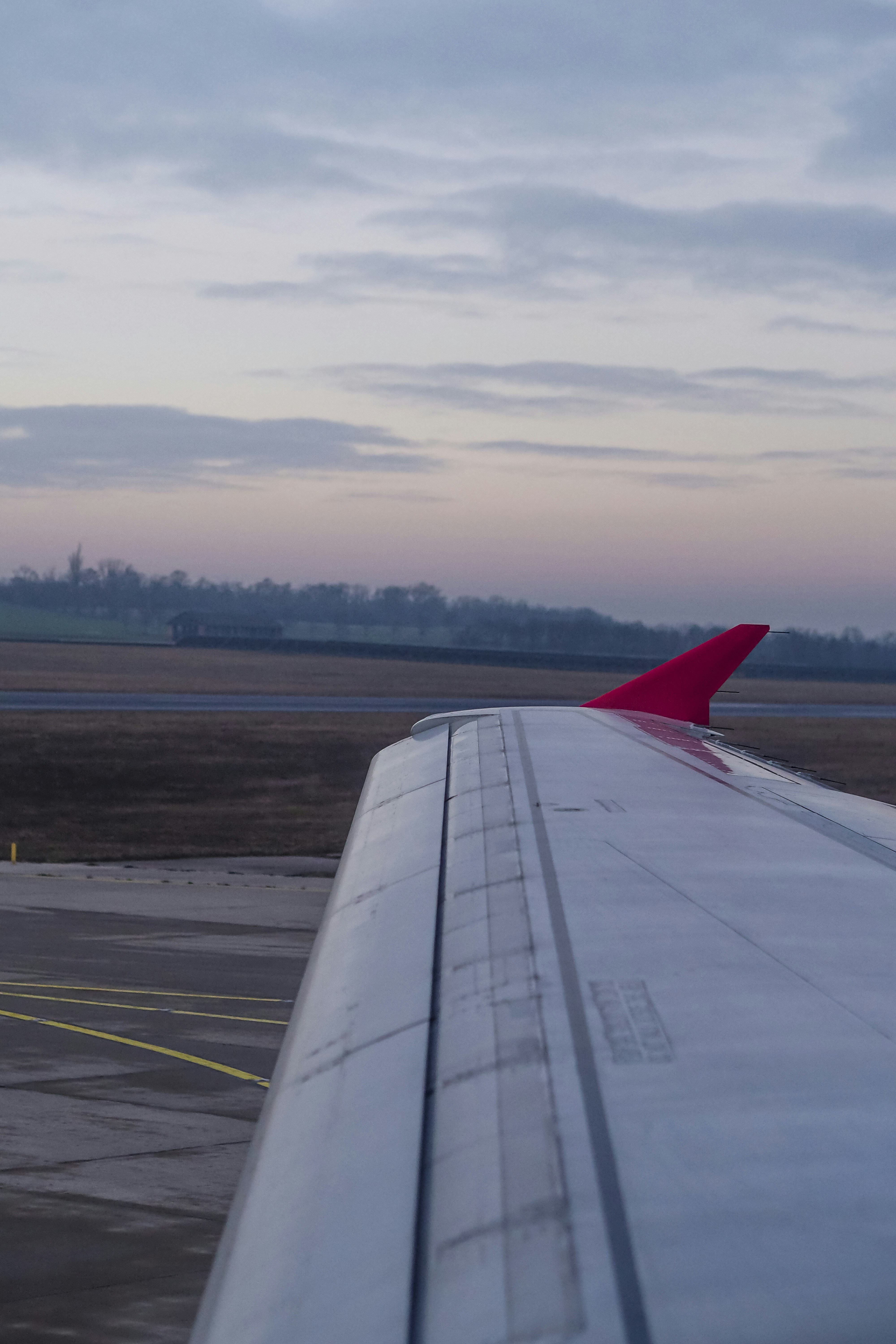 An airplane wing with a red winglet above an airport runway at low light