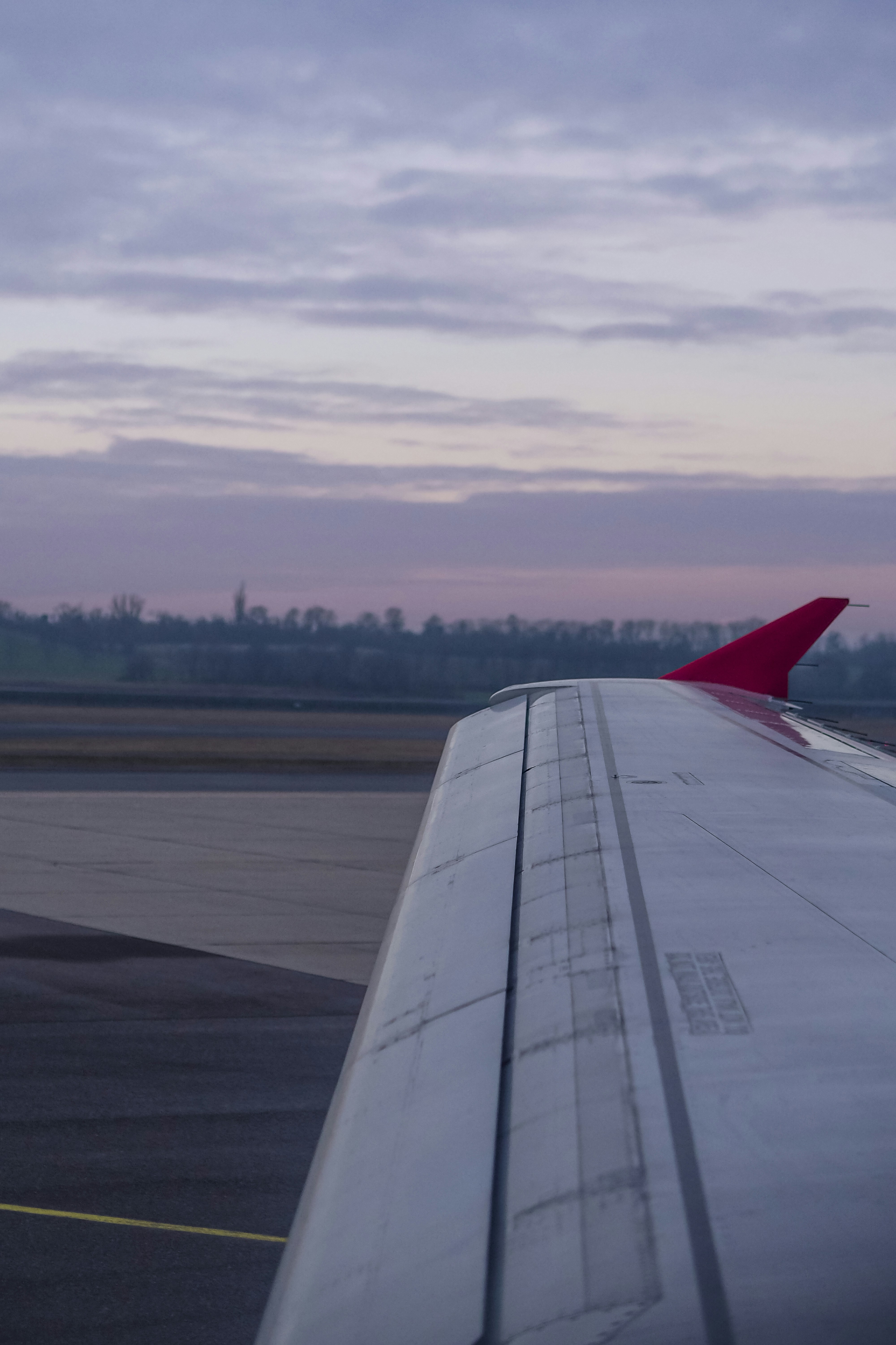 An airplane wing with a red winglet against a soft purple sky