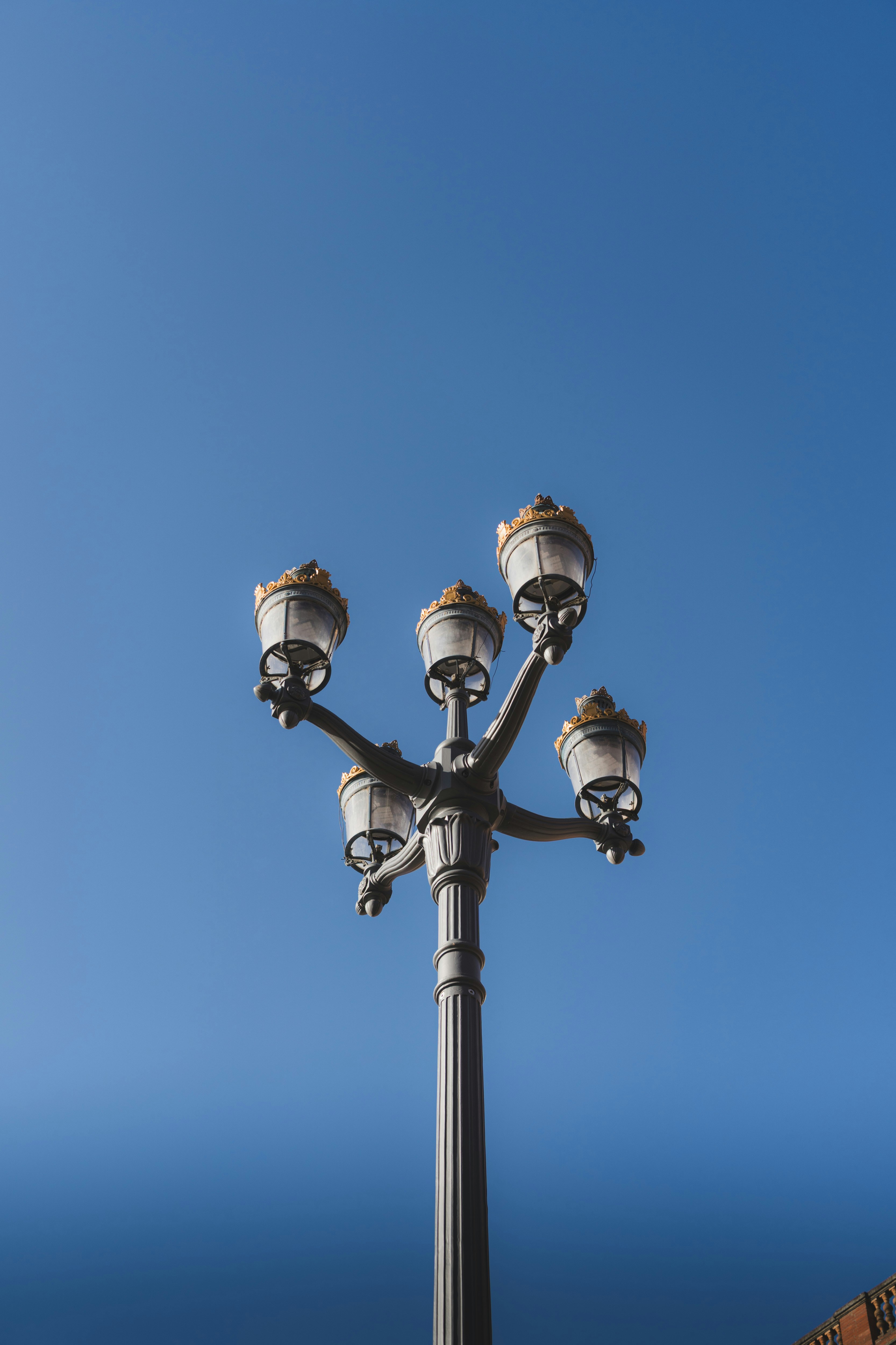 An ornate street lamp with four glass lanterns against a clear blue sky