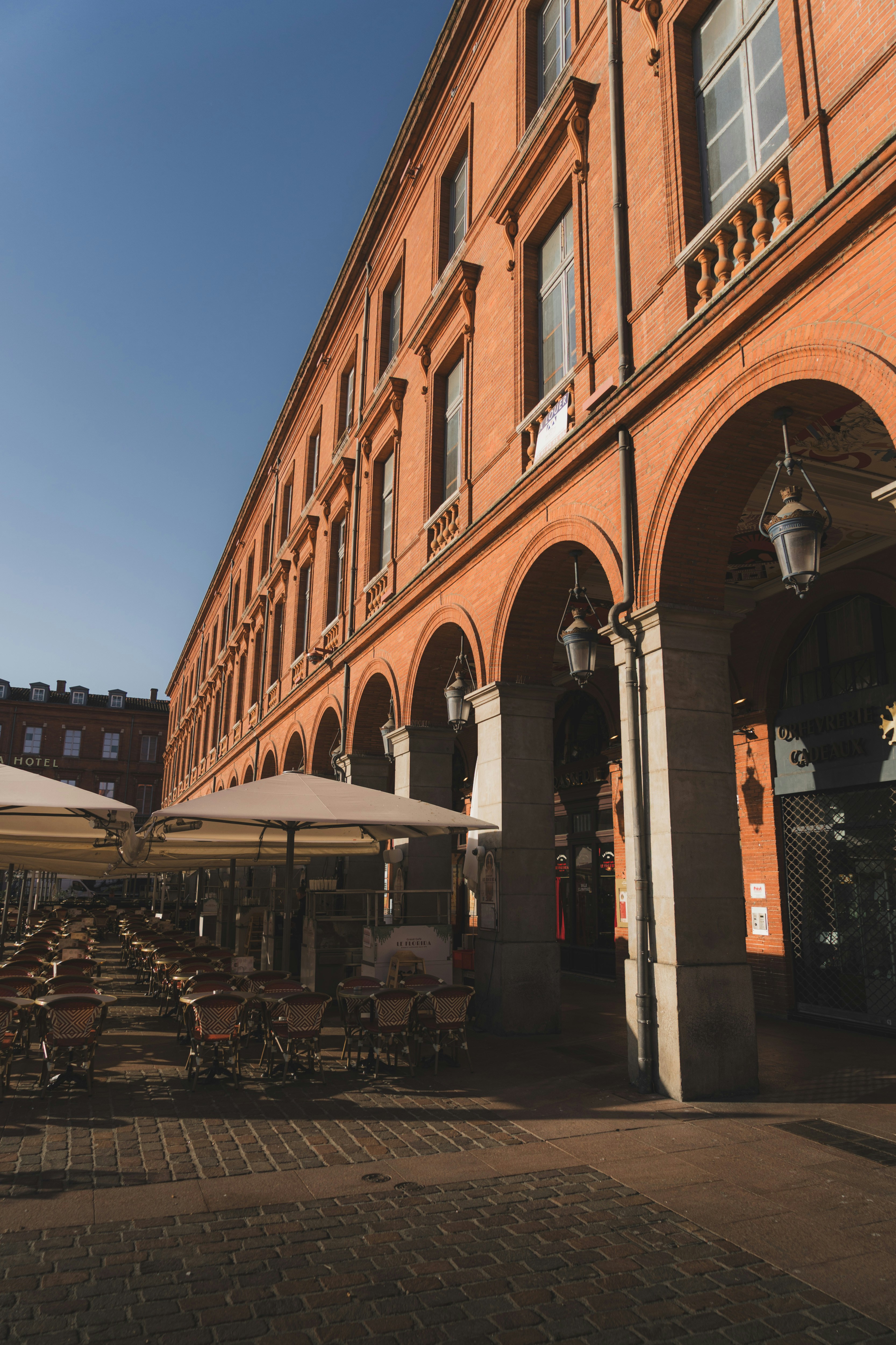 Outdoor cafe tables and umbrellas under the arched brick arcade of a building
