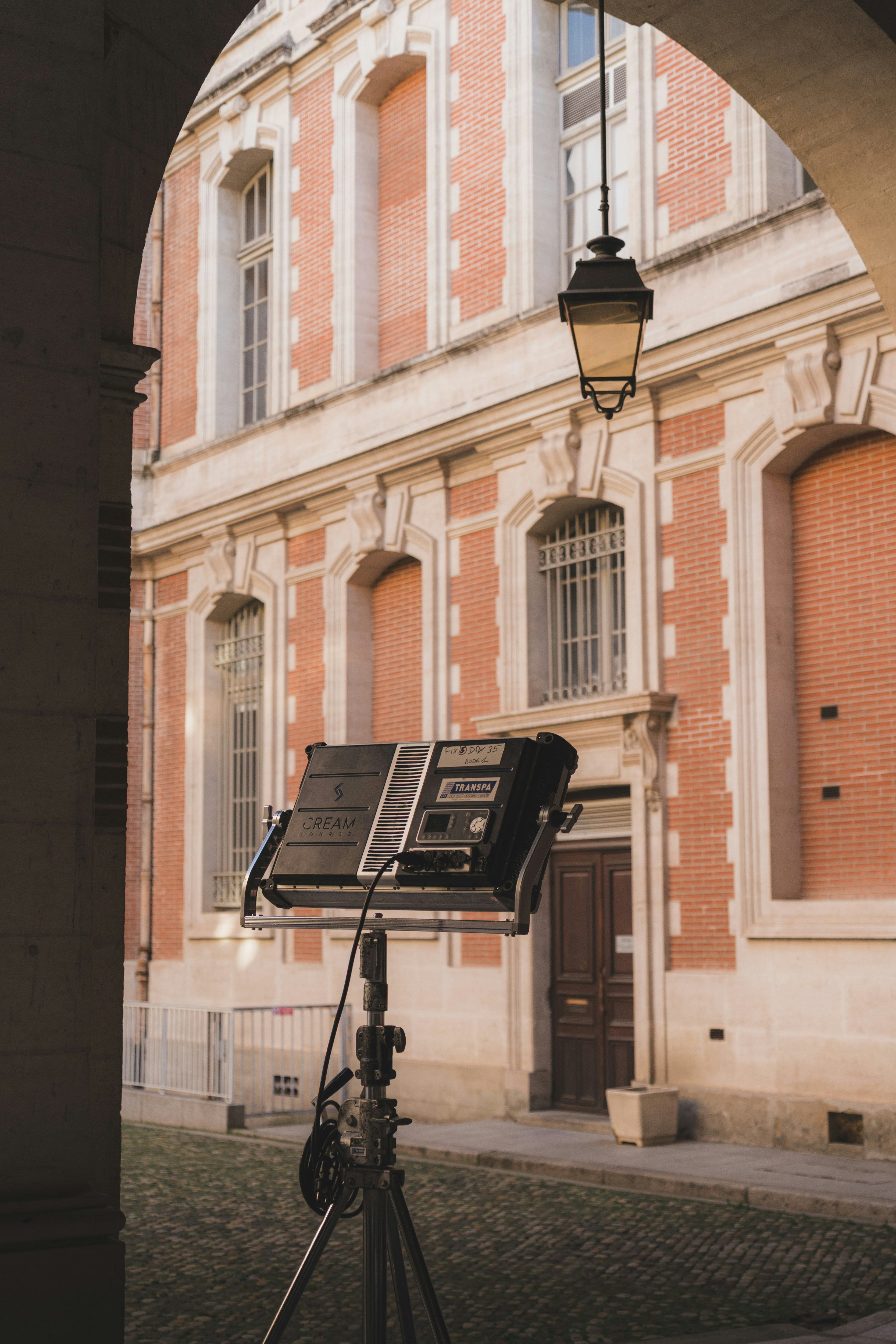 A professional film lighting panel on a tripod in a historic brick courtyard