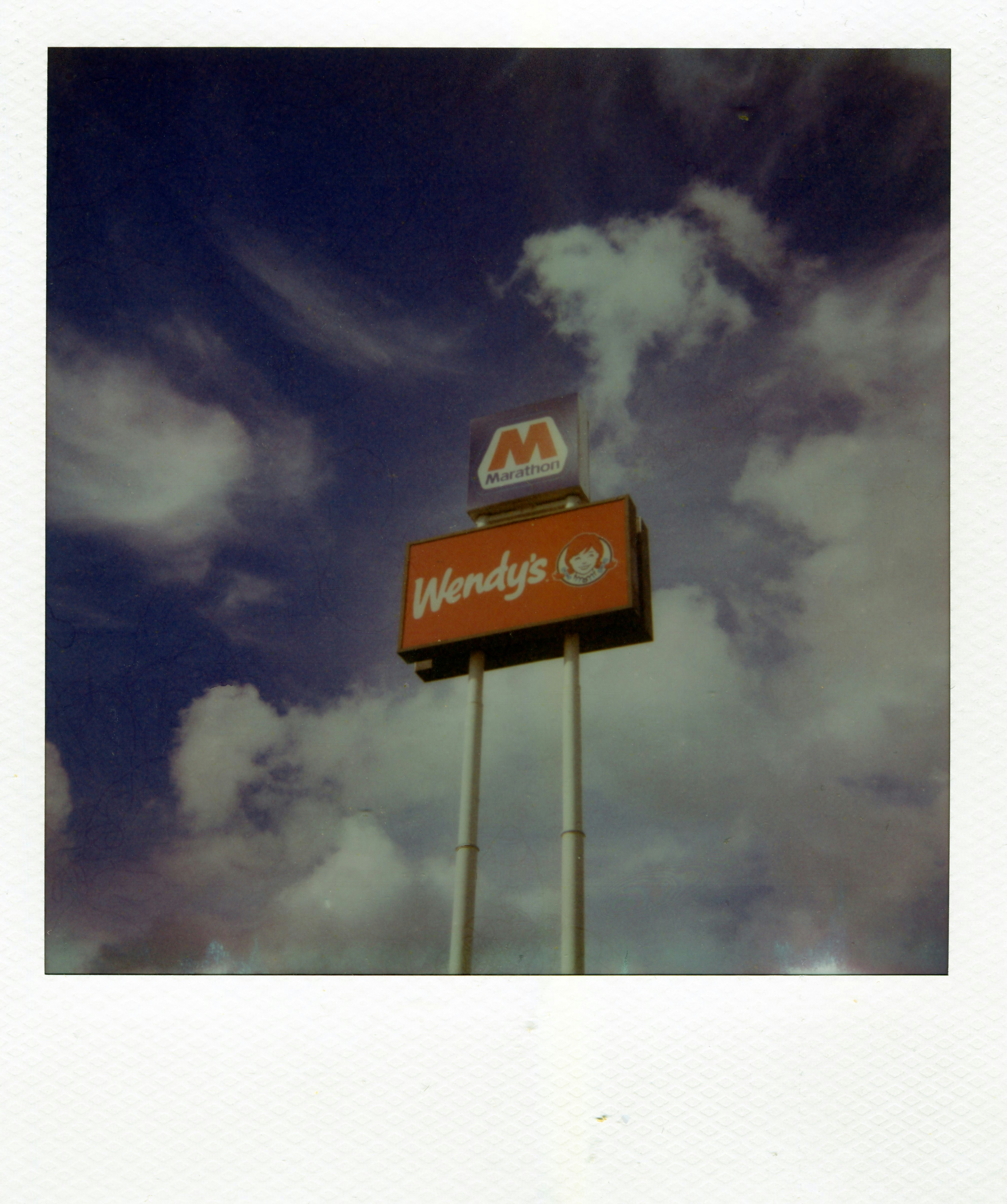 A Wendy's and Marathon sign on tall poles against a cloudy blue sky