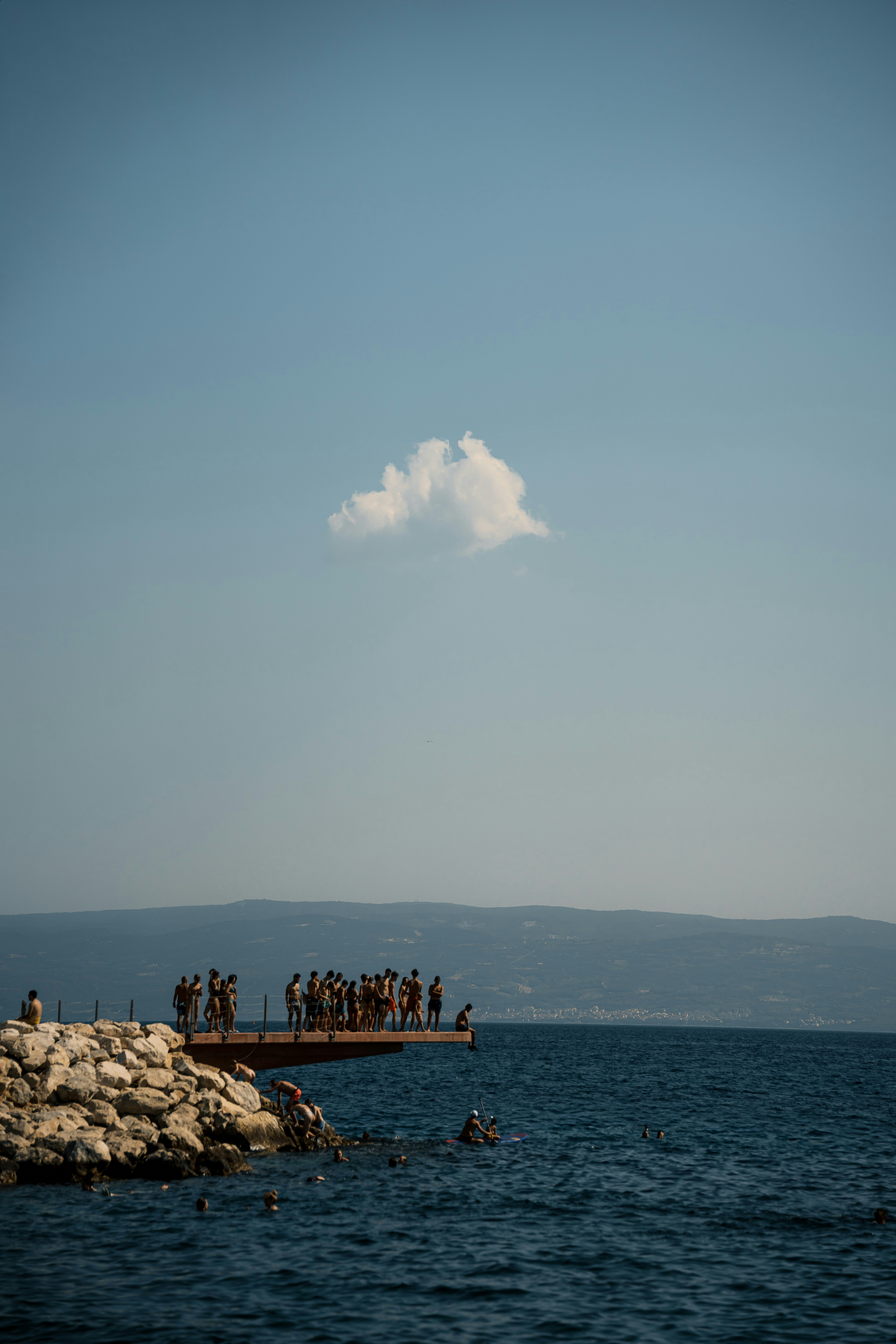 A group of people on a pier extending into the sea under a single cloud
