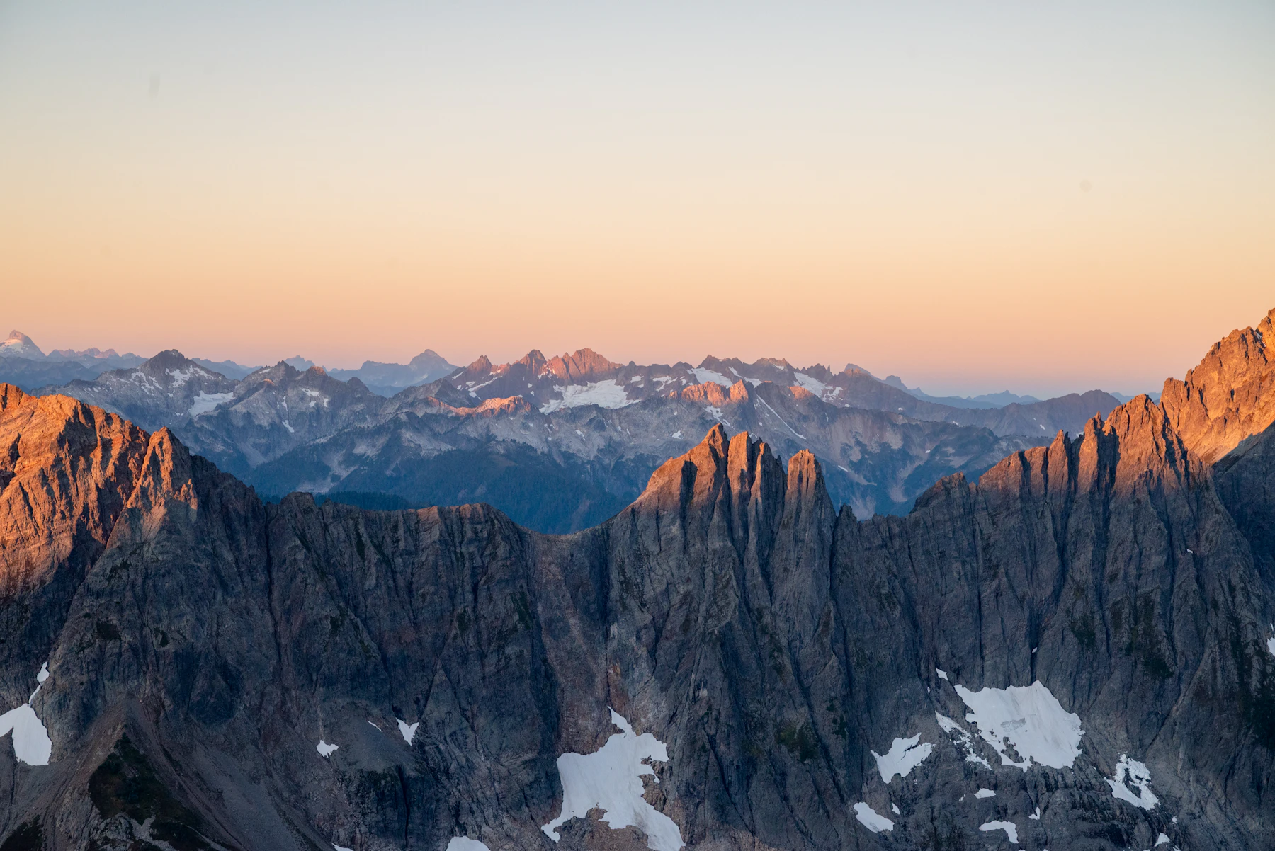 Jagged mountain peaks under a soft orange sky at golden hour