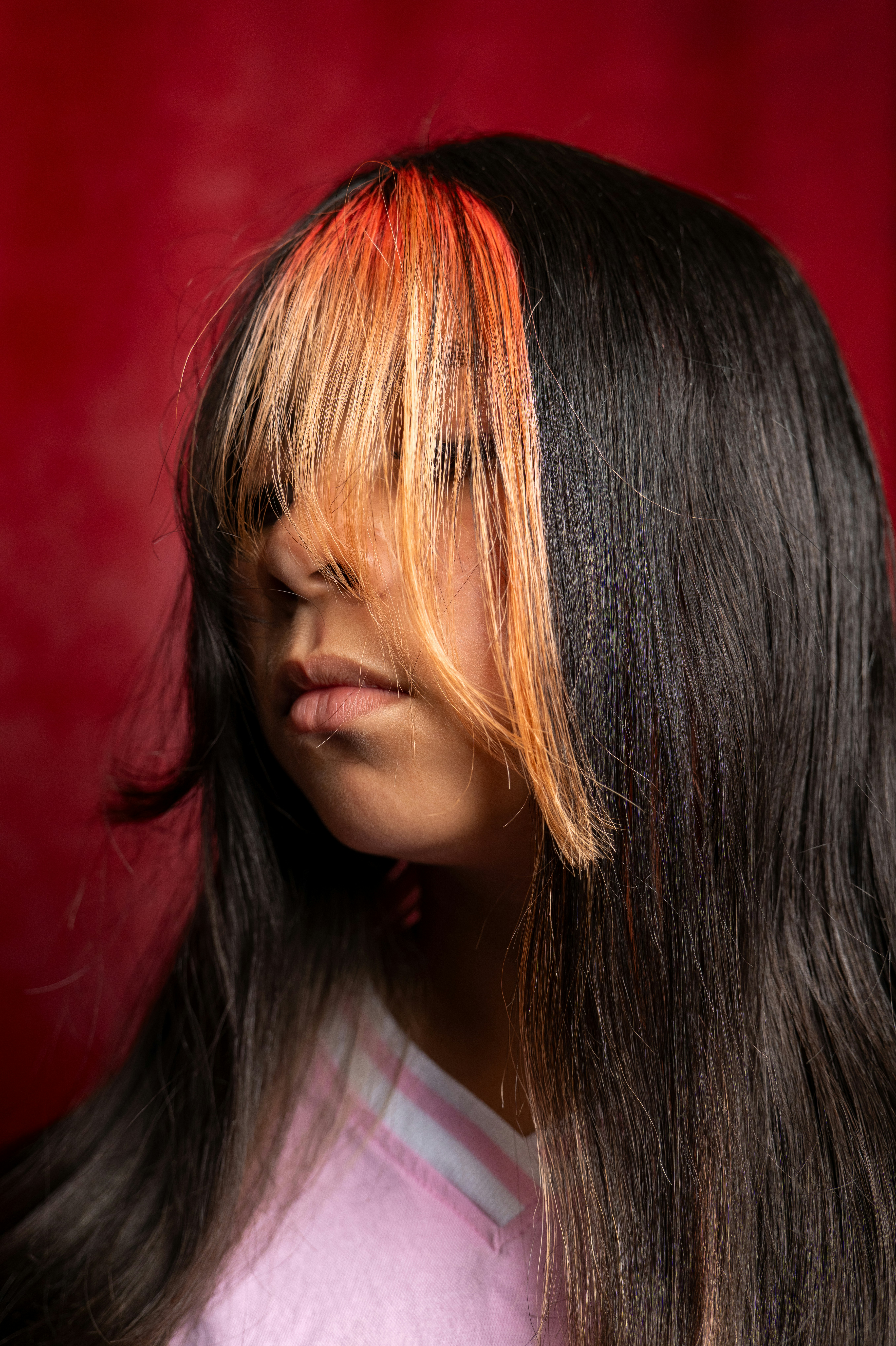 A person with long dark hair and orange highlights covering their eyes