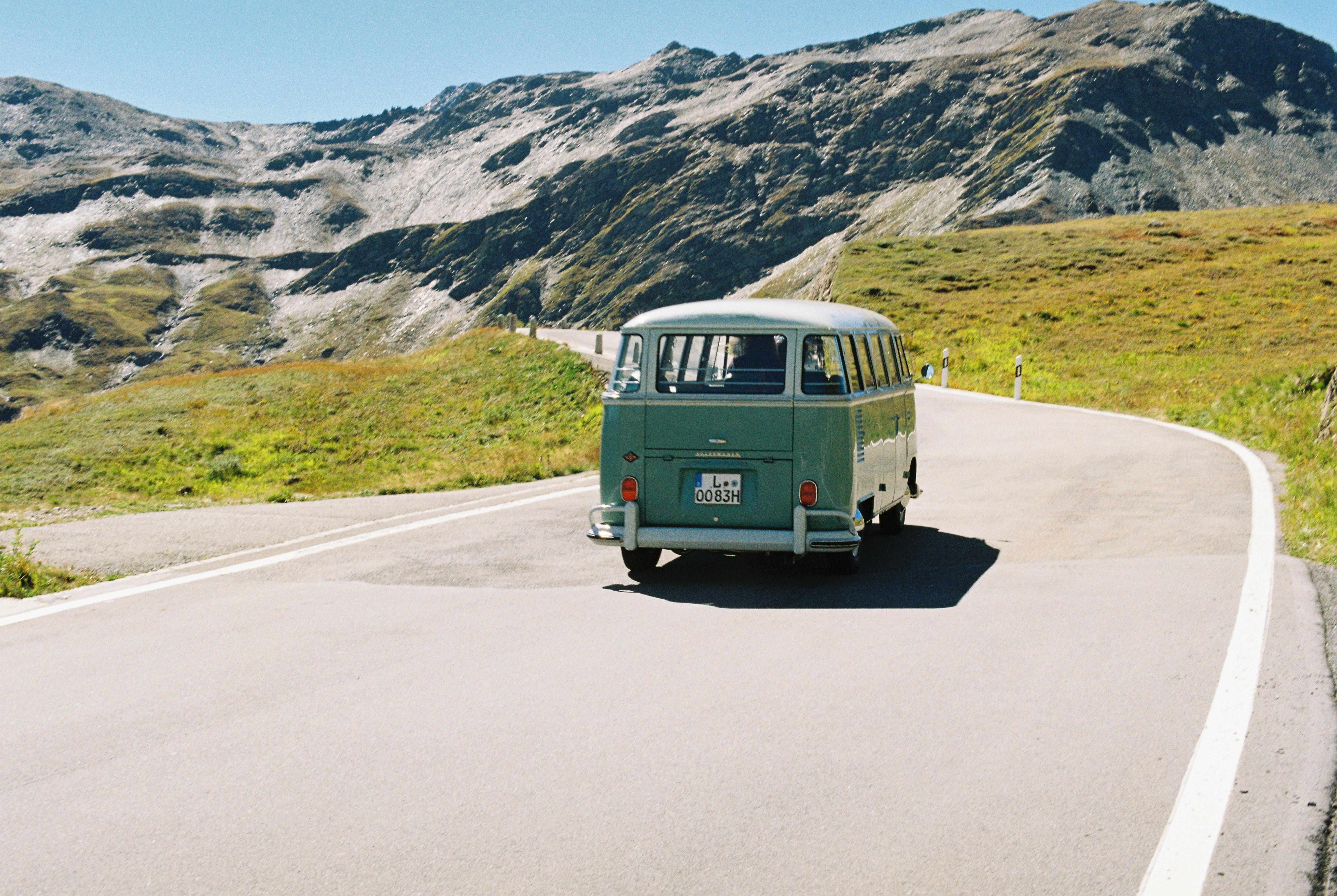 A light green vintage Kombi driving on a winding mountain road