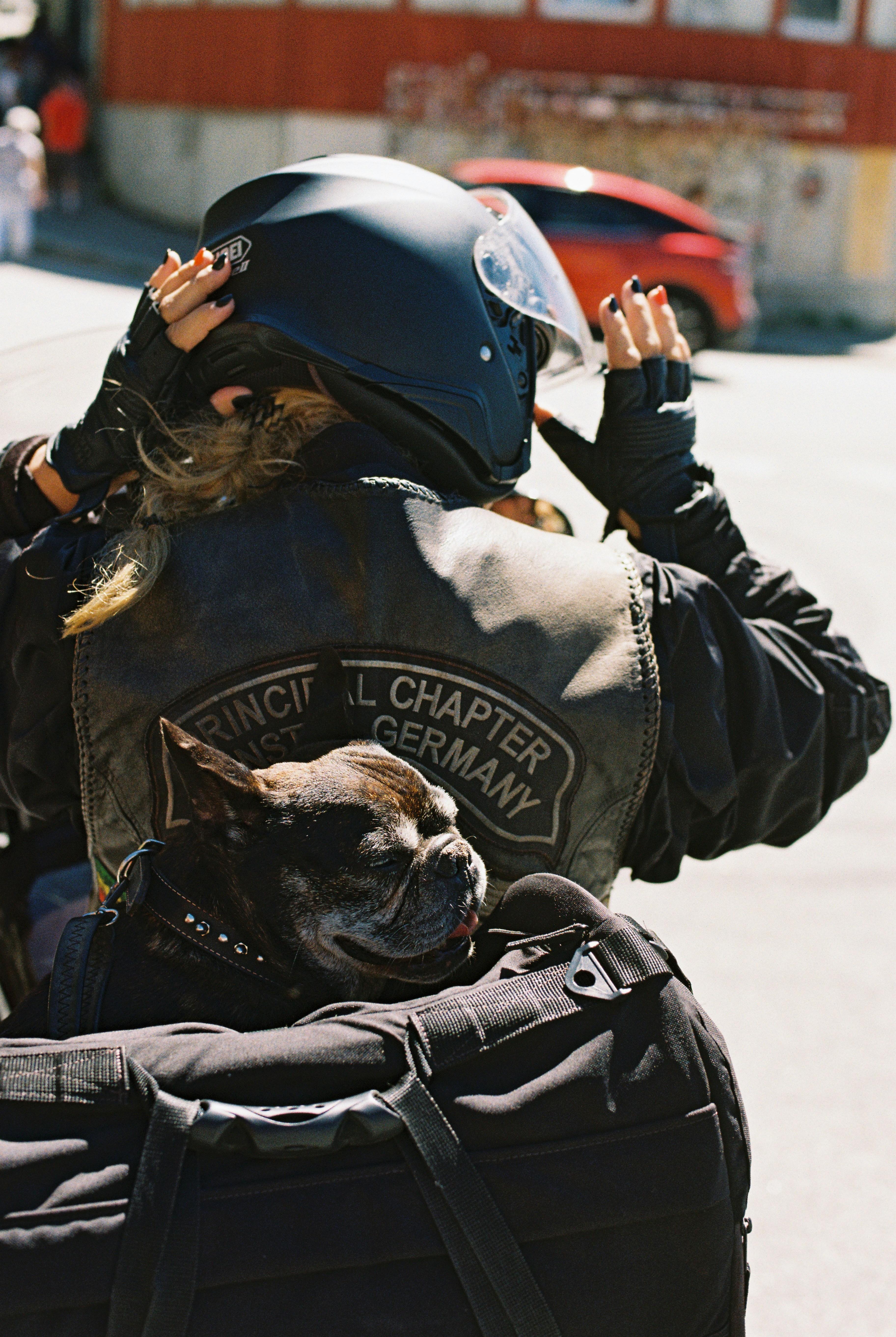 A person wearing a helmet and leather vest with a dog in a backpack