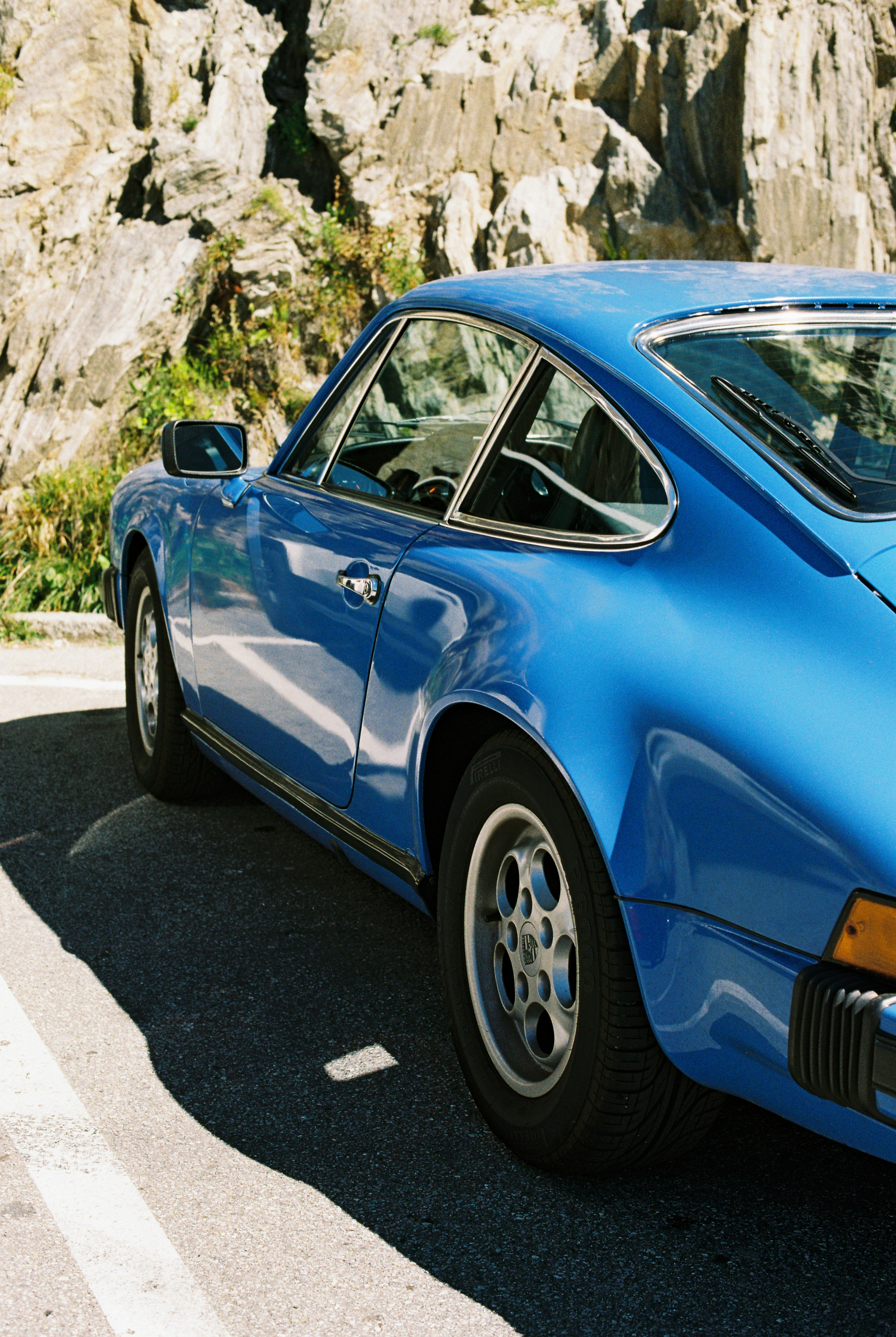 A blue vintage sports car parked on a road beside a rocky cliff