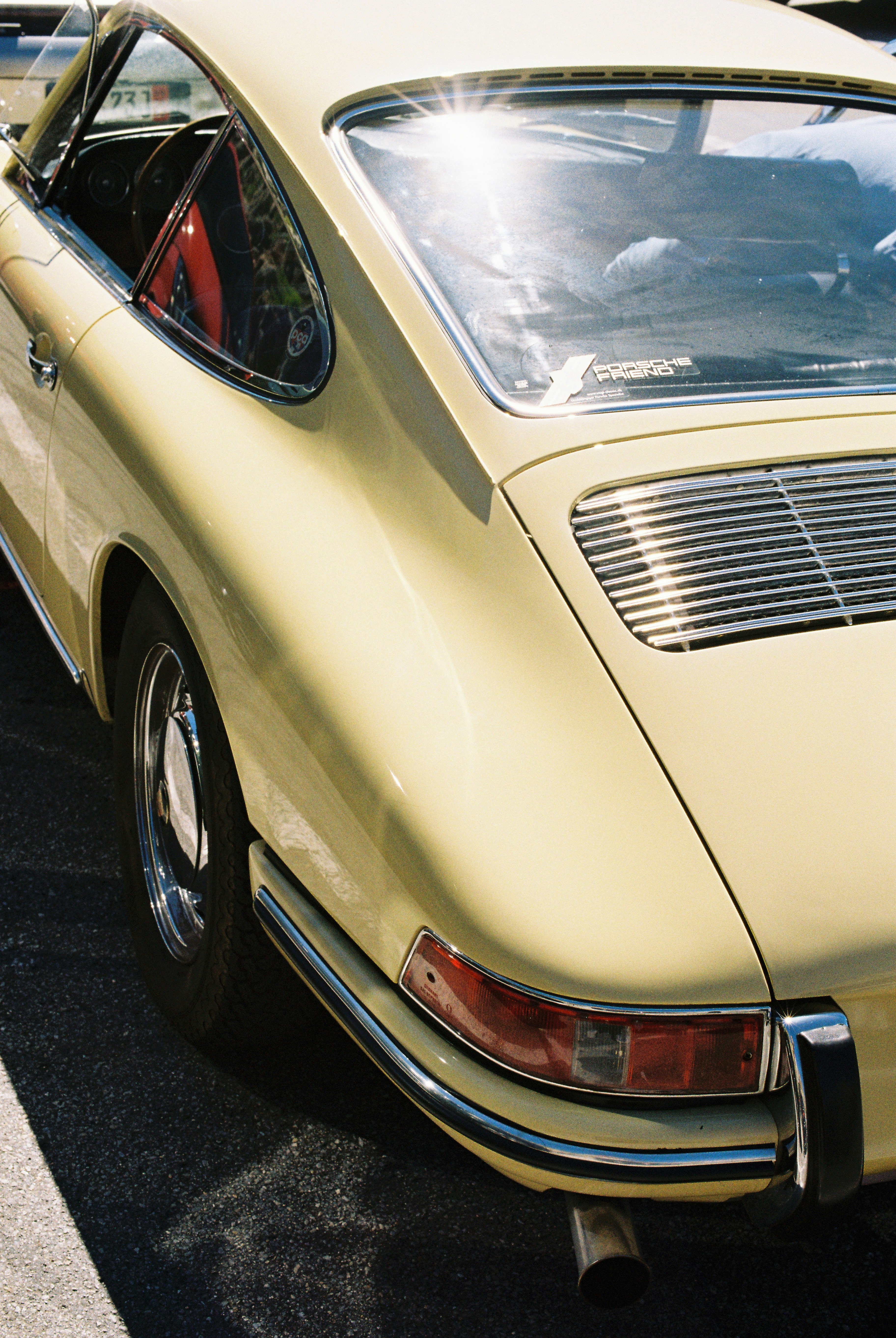 A vintage pale yellow sports car parked on asphalt in bright sunlight