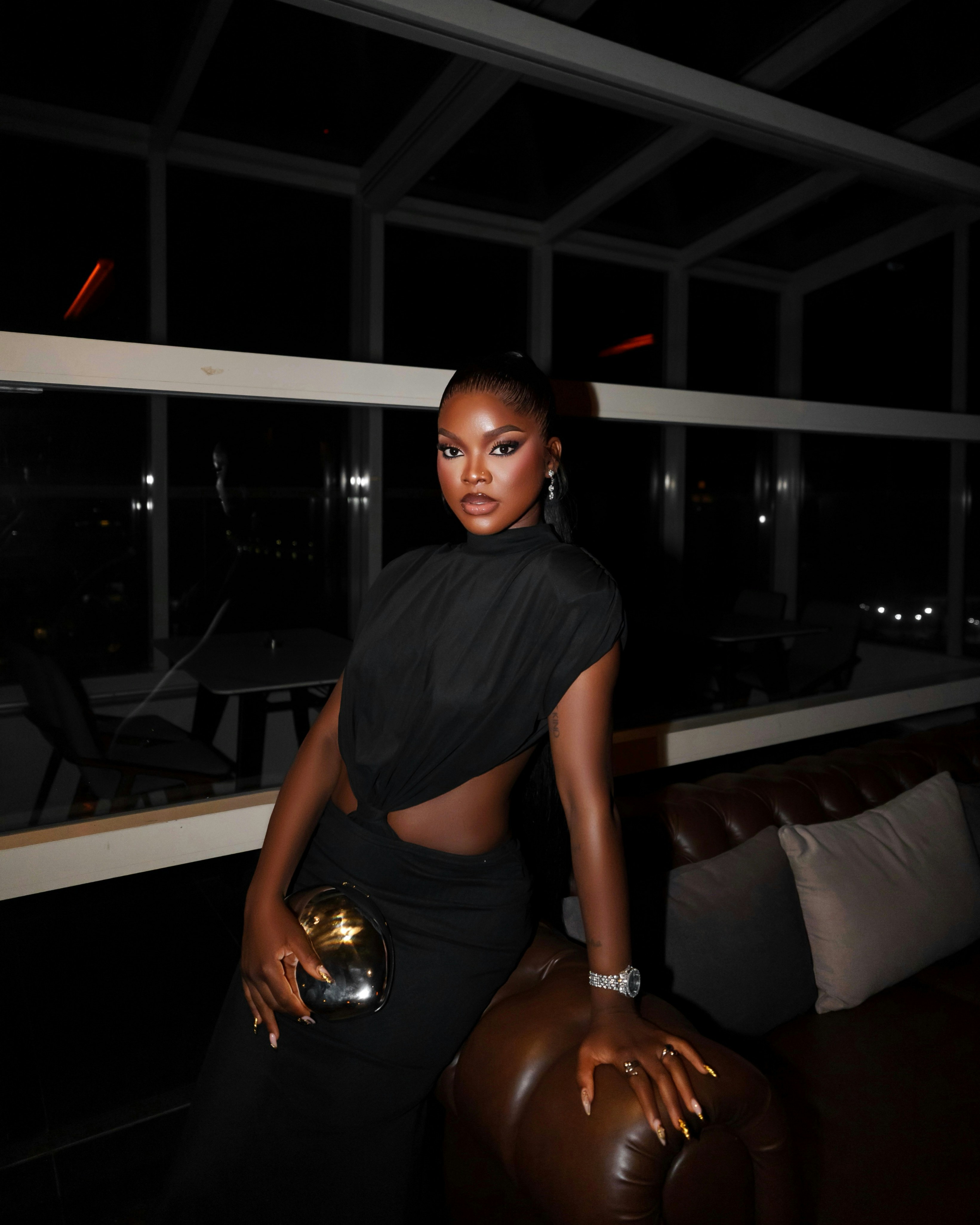 A woman in a black cutout dress holding a metallic clutch in a lounge