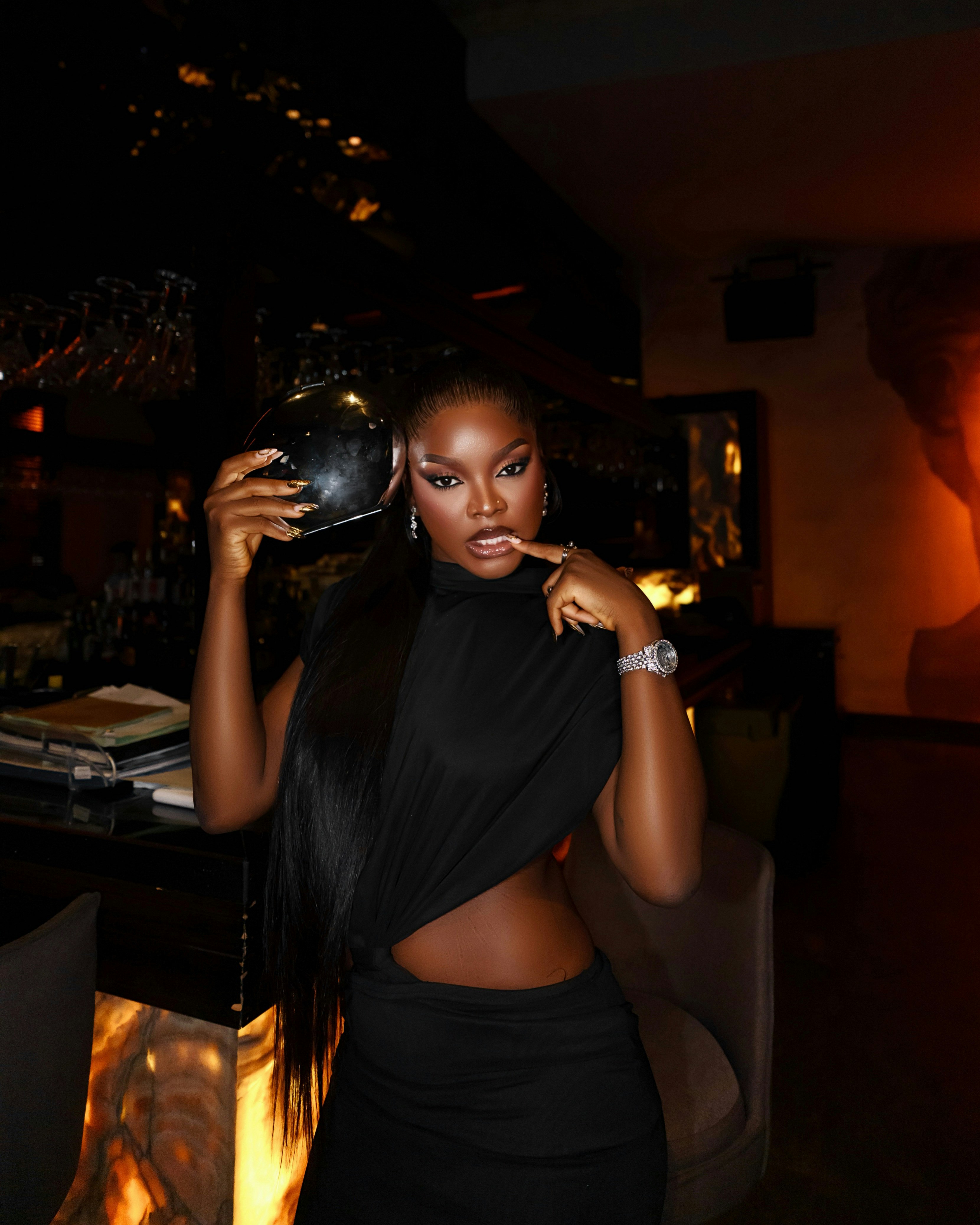 A woman in a black dress holding a small clutch in a dimly lit bar