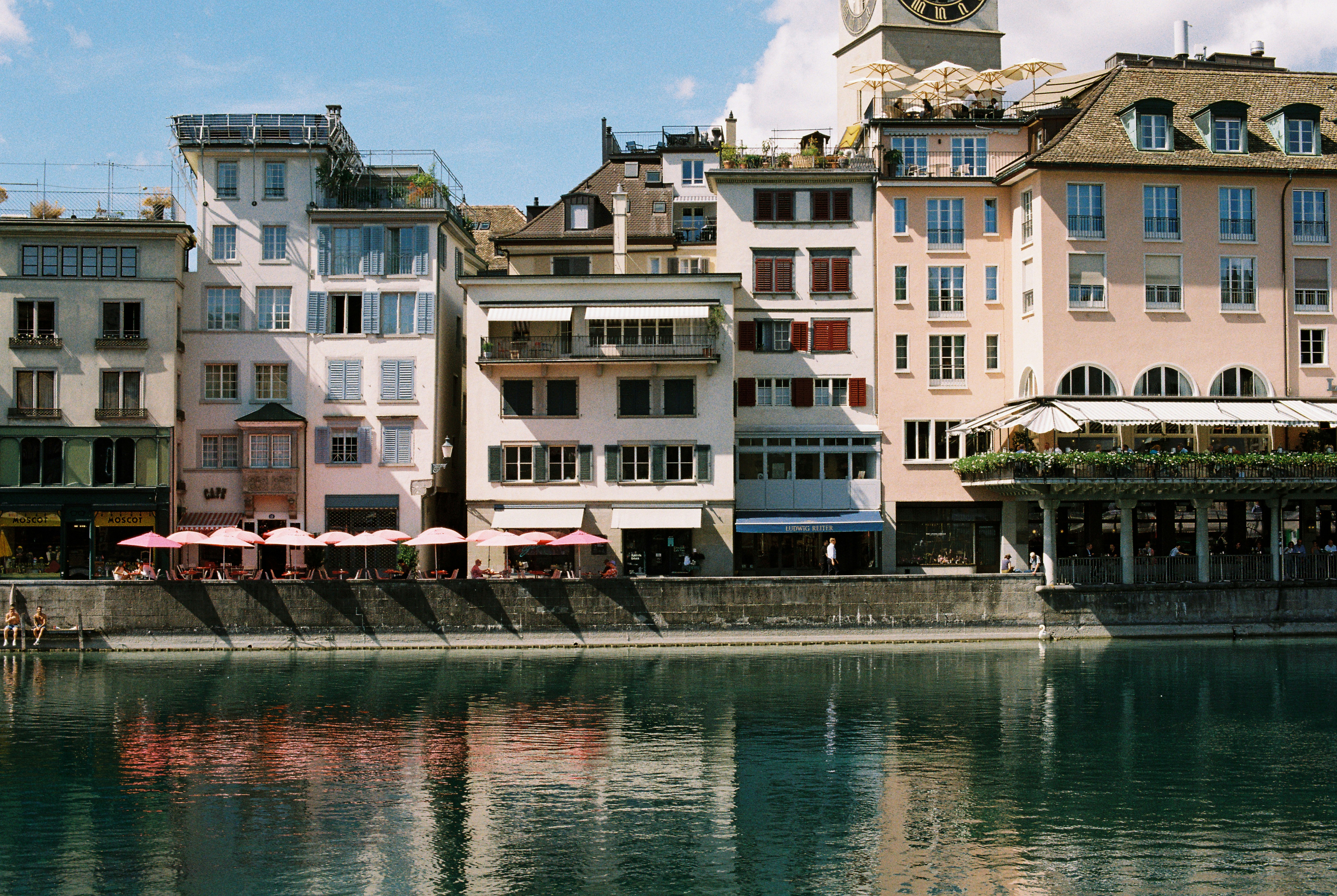 Multi-story buildings with pink umbrellas along the Limmat river in Zurich