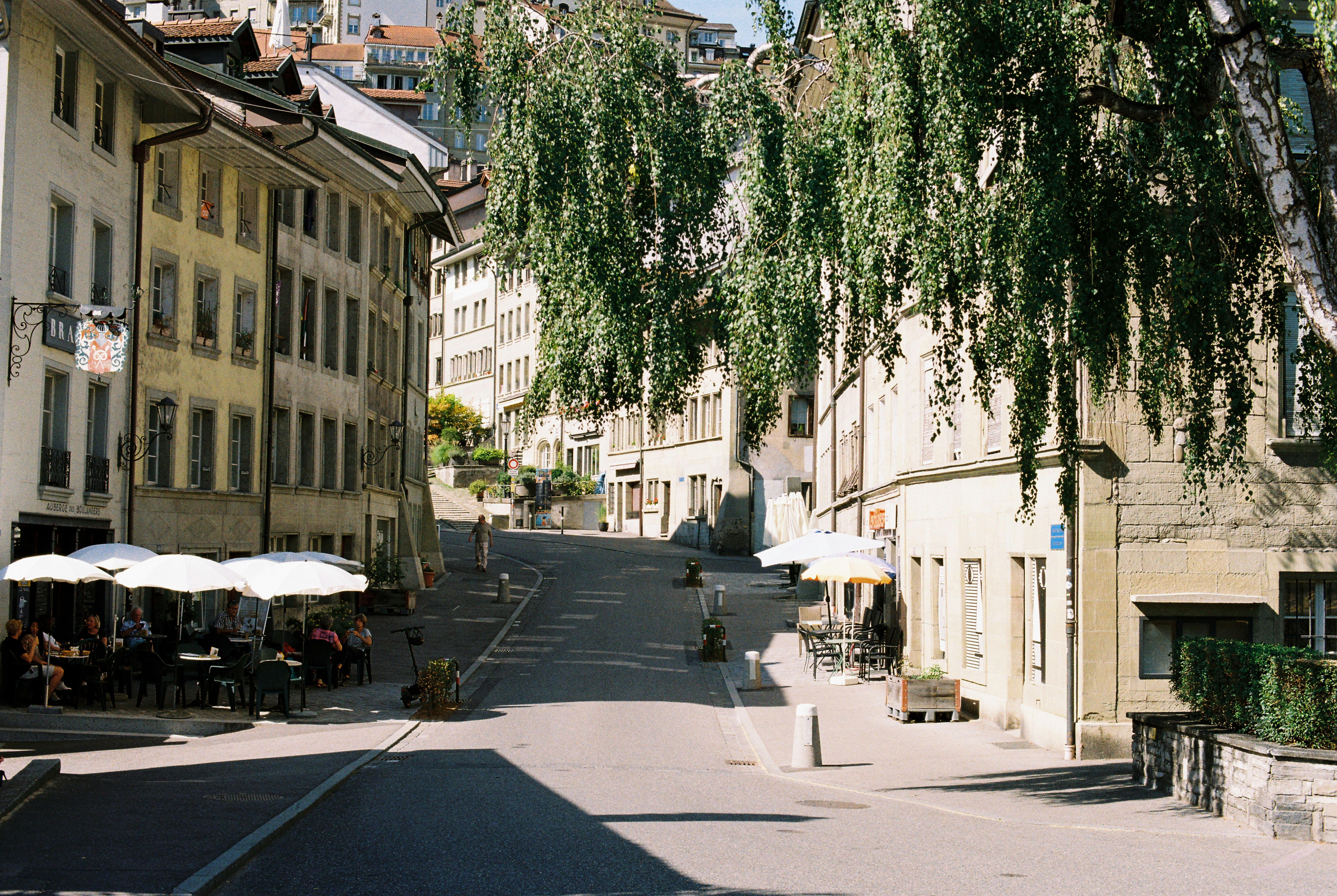 A quiet street in Fribourg with outdoor cafe seating under white umbrellas