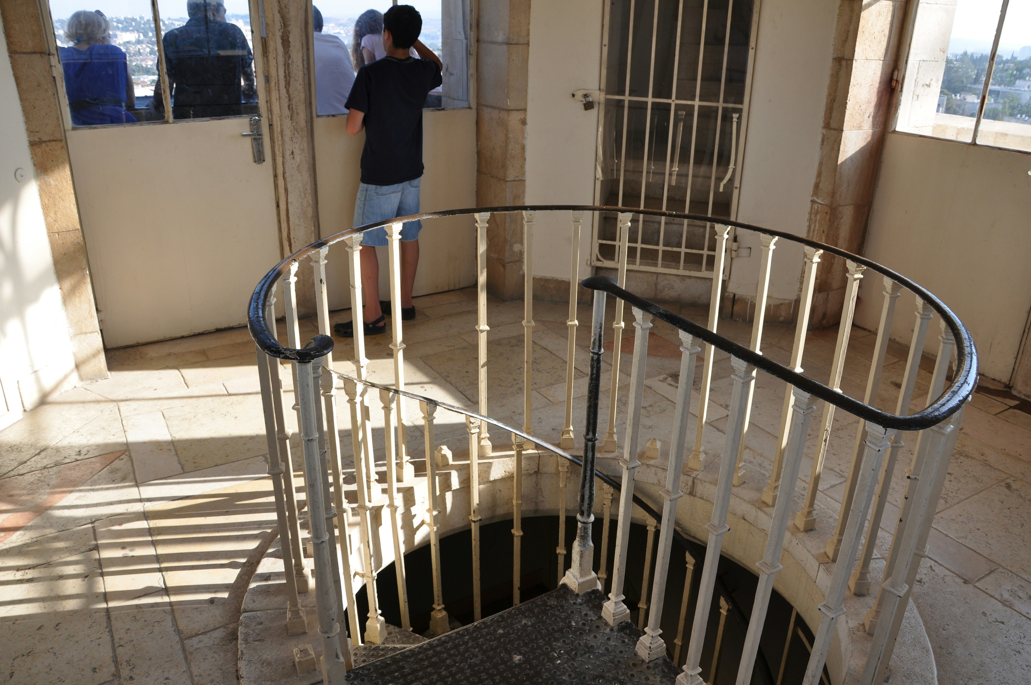 A spiral staircase with a metal railing inside a stone tower with people looking out