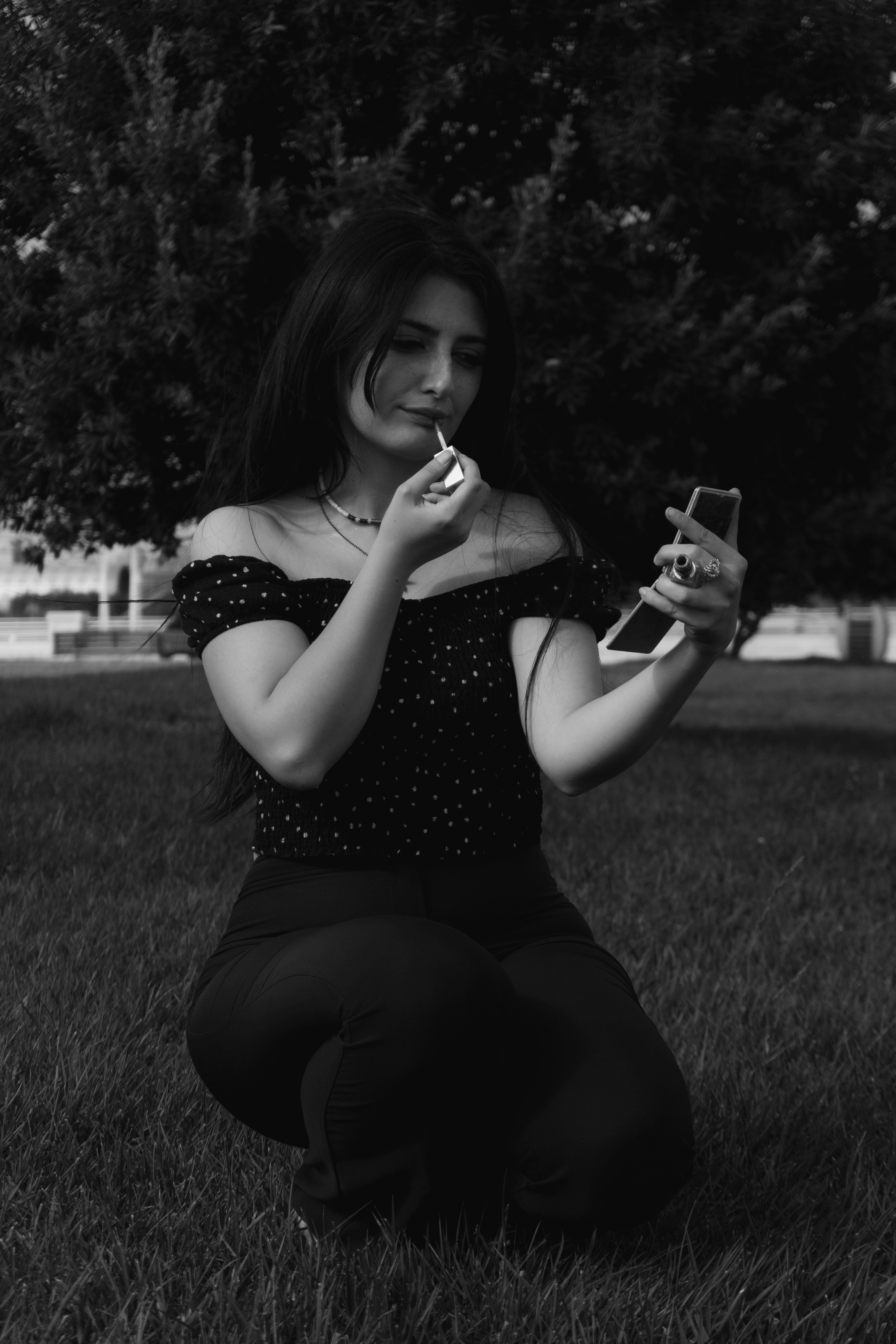 A woman in a polka dot top applying lip gloss in a park