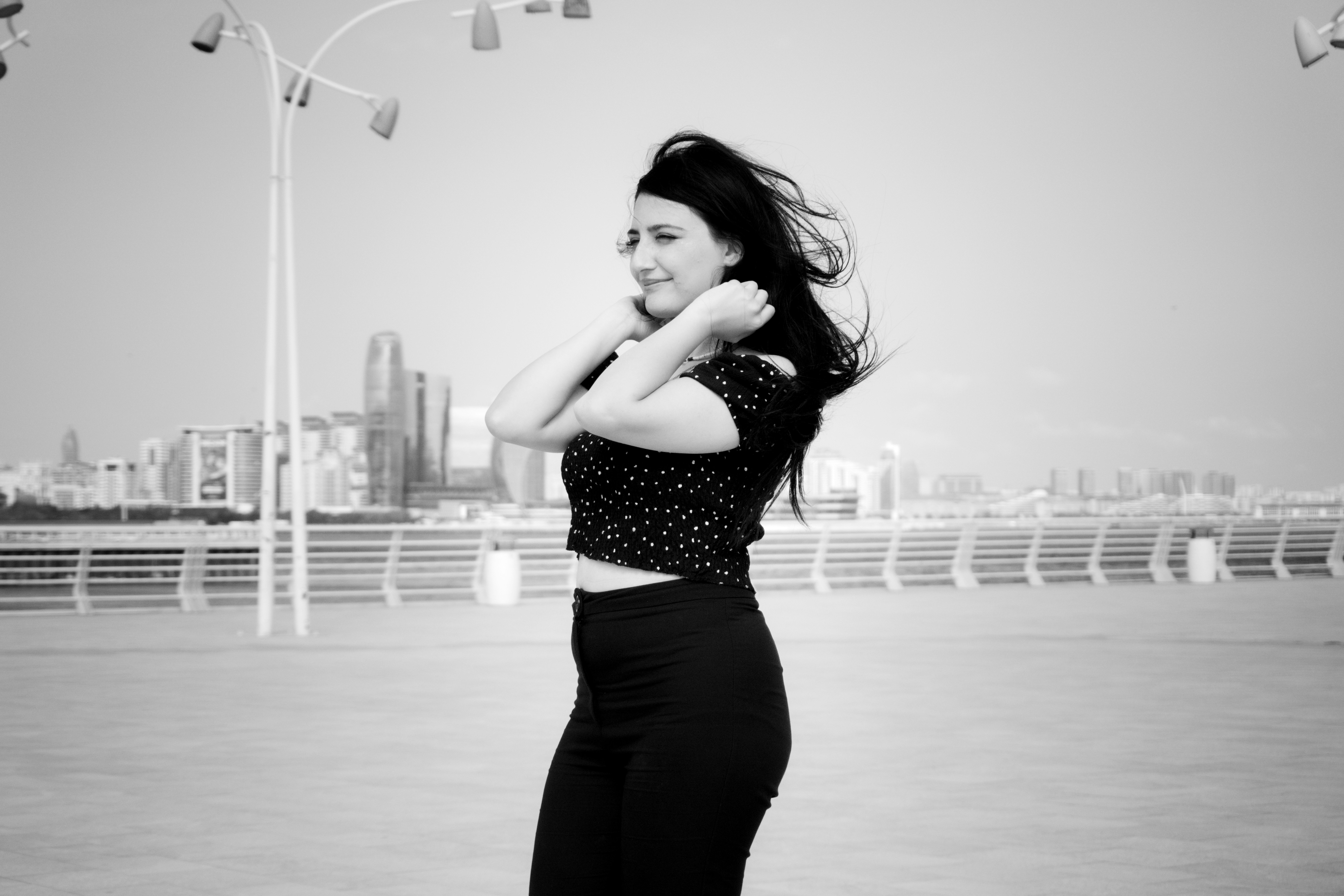 A woman in a polka dot top touching her hair on a city waterfront
