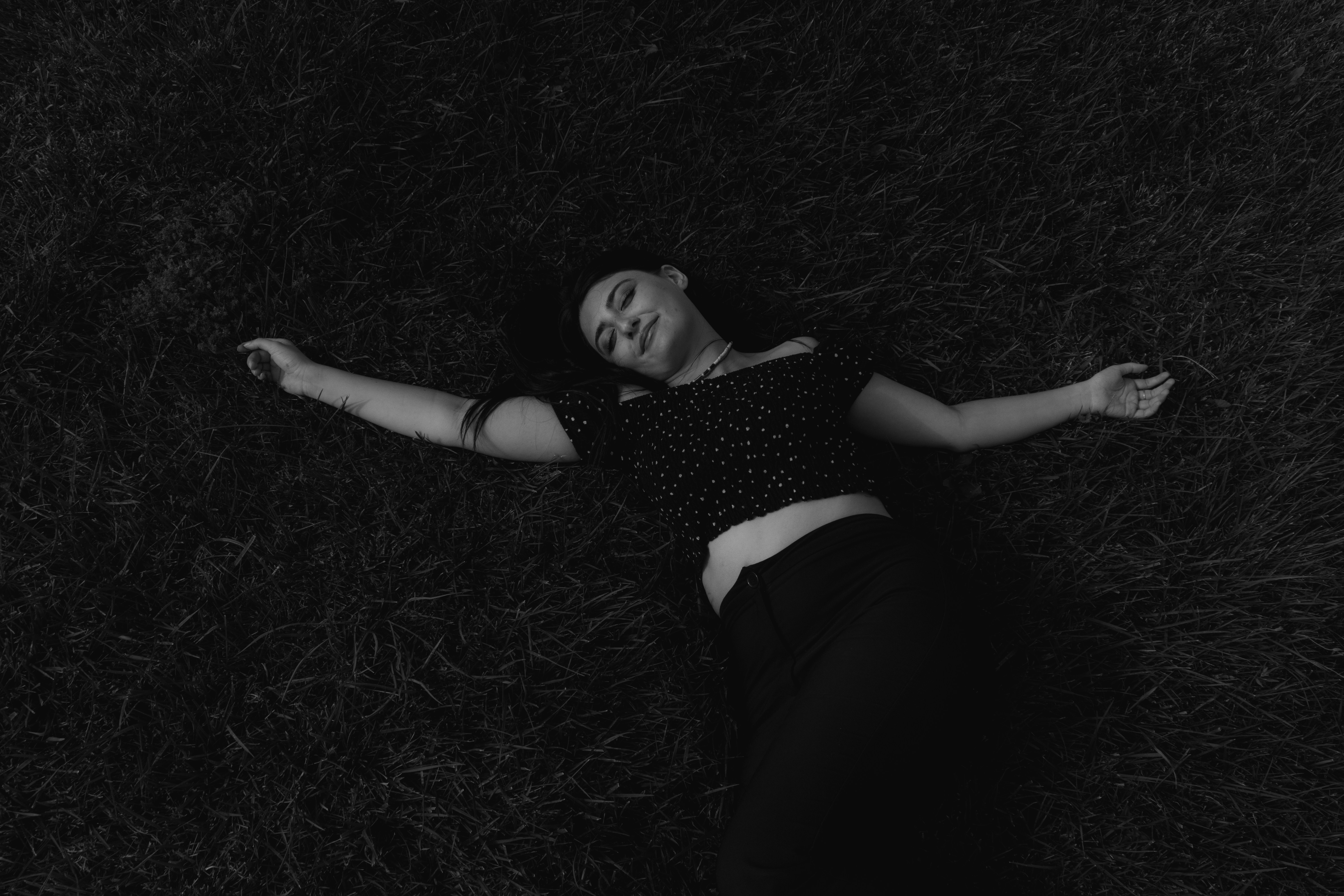 A woman in a polka dot top lying on grass with arms outstretched