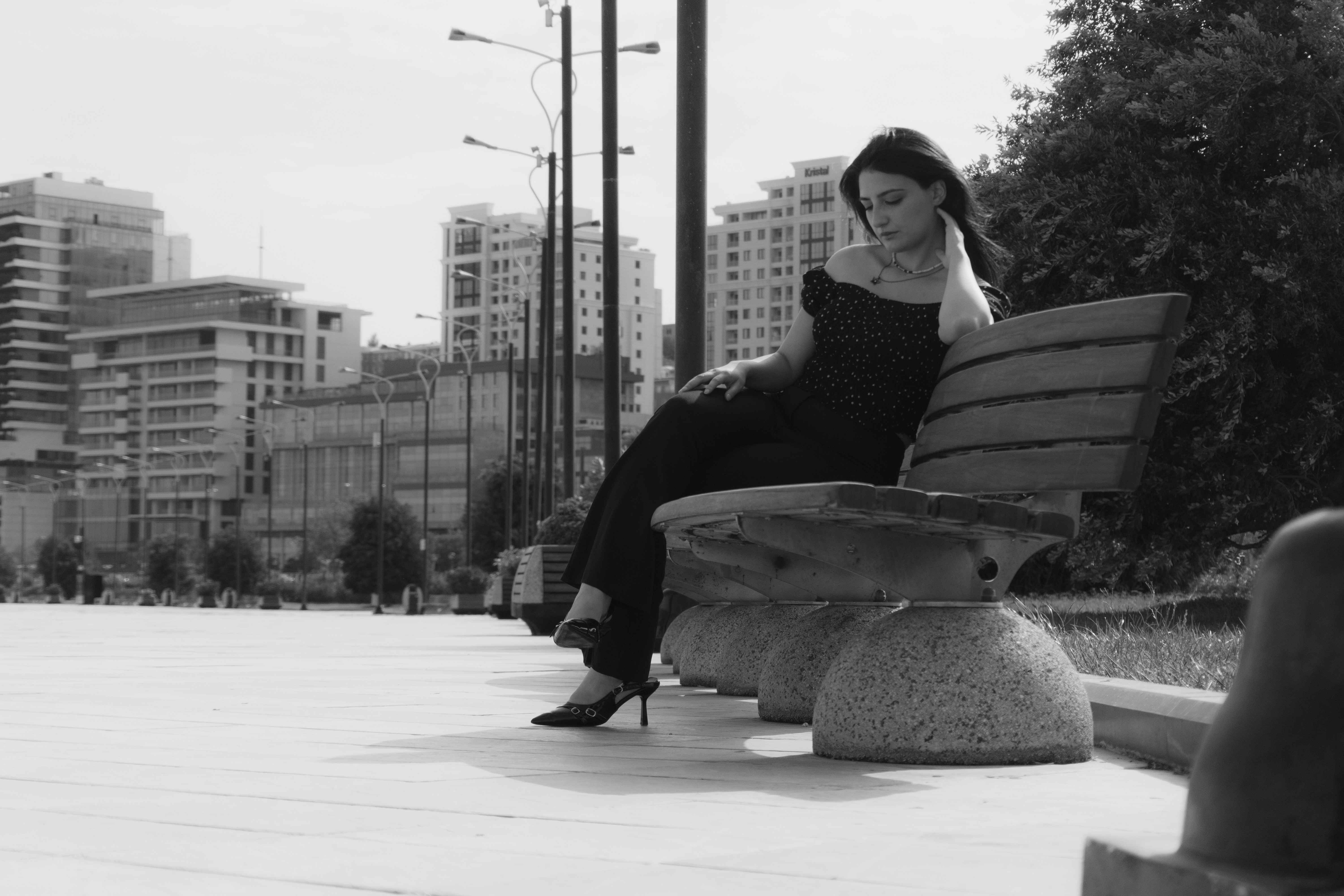 A woman in a polka dot top on a bench in a city park