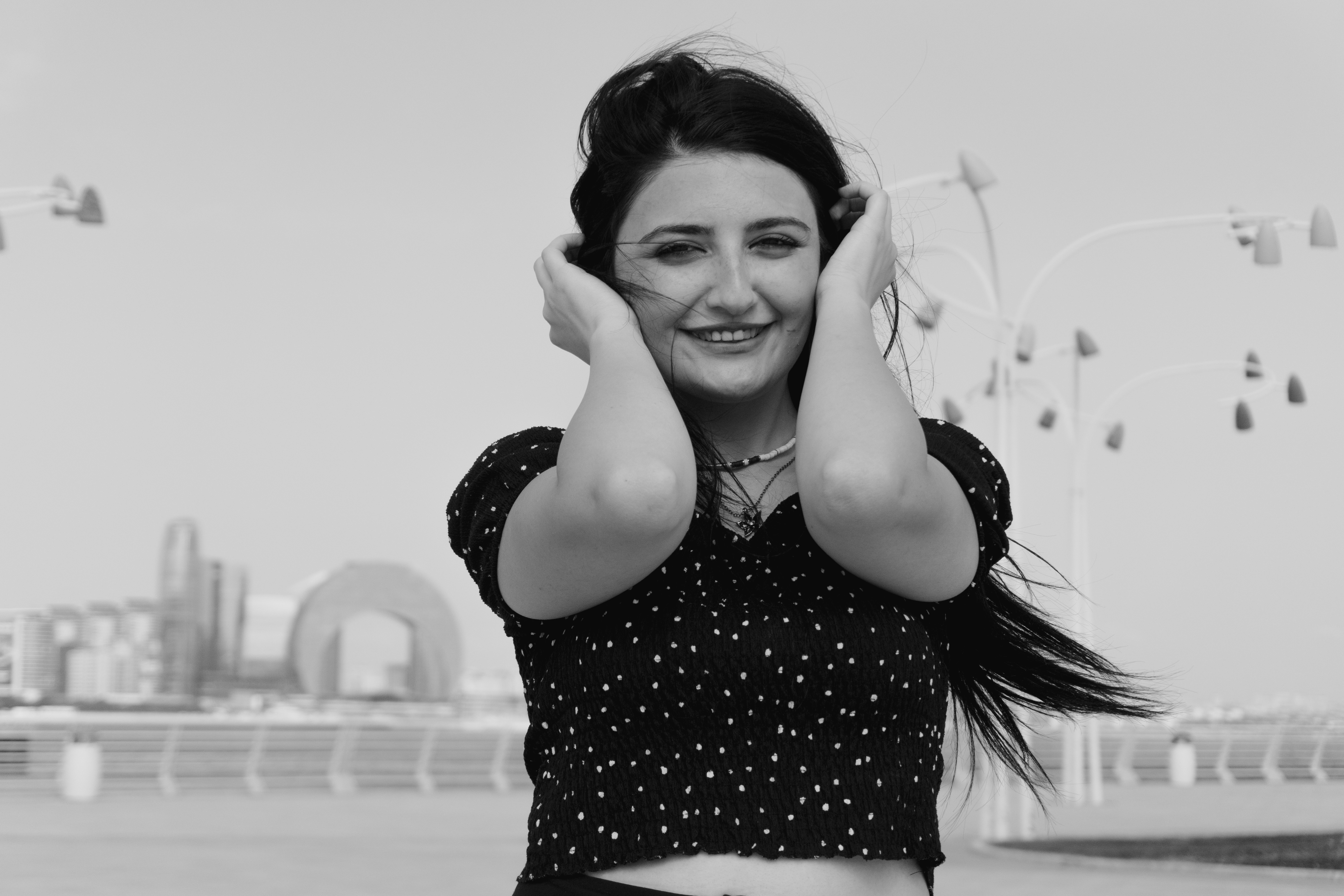 A woman in a polka dot top holding her hair on a waterfront promenade