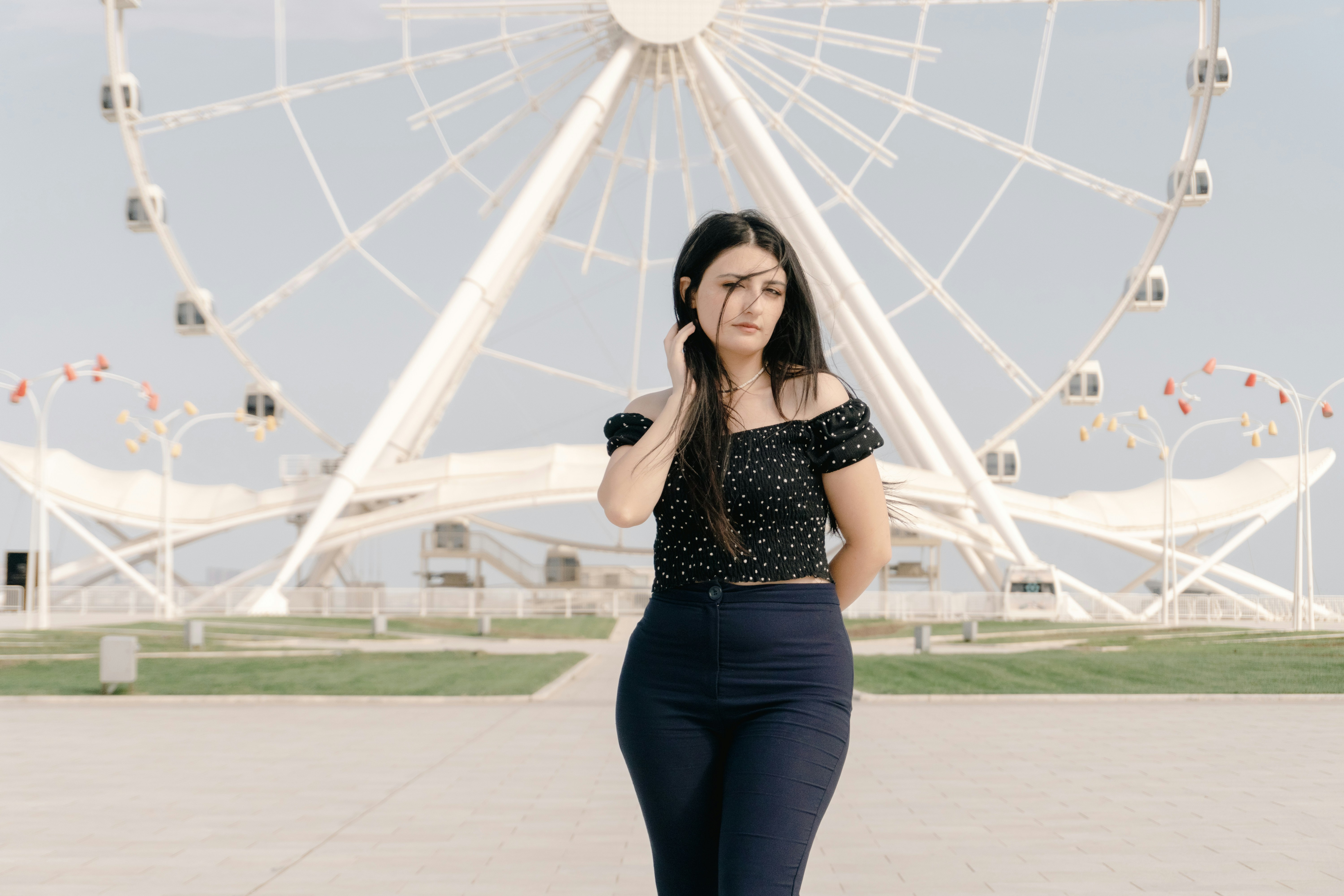 A woman in a black polka dot top before a large white ferris wheel