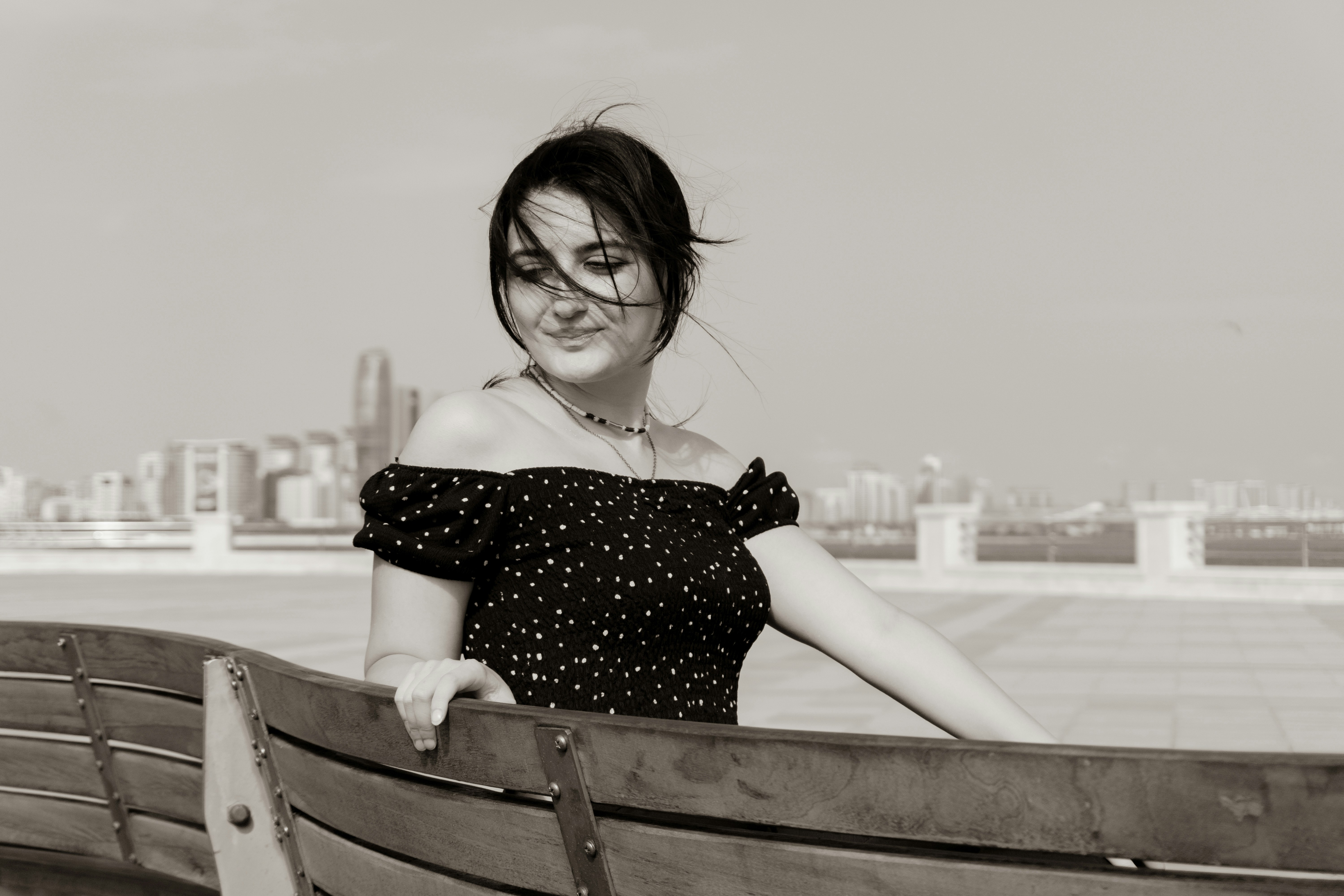 A woman in a black polka dot top leaning on a wooden bench