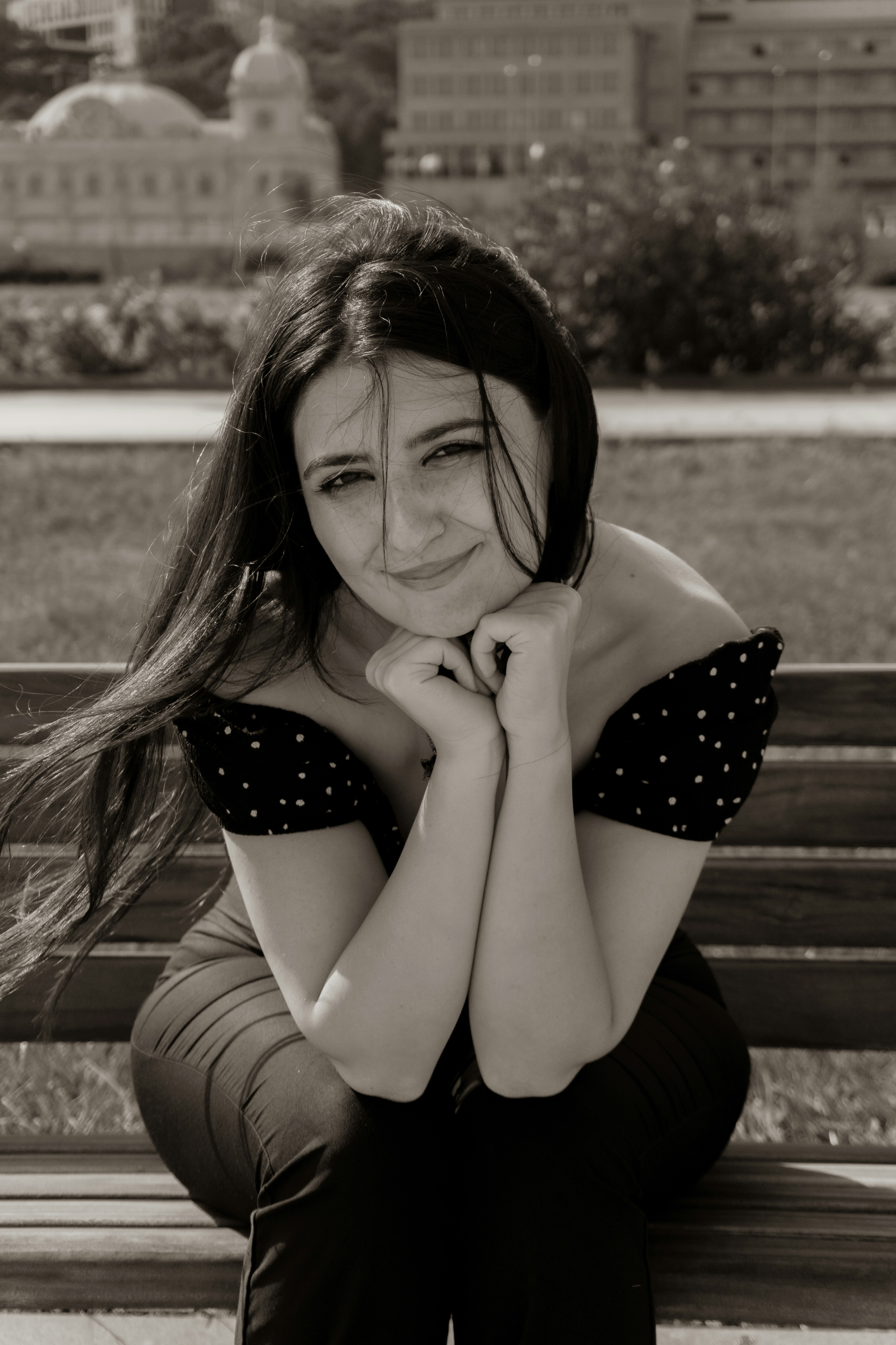 A woman with long dark hair in a polka dot top on a park bench