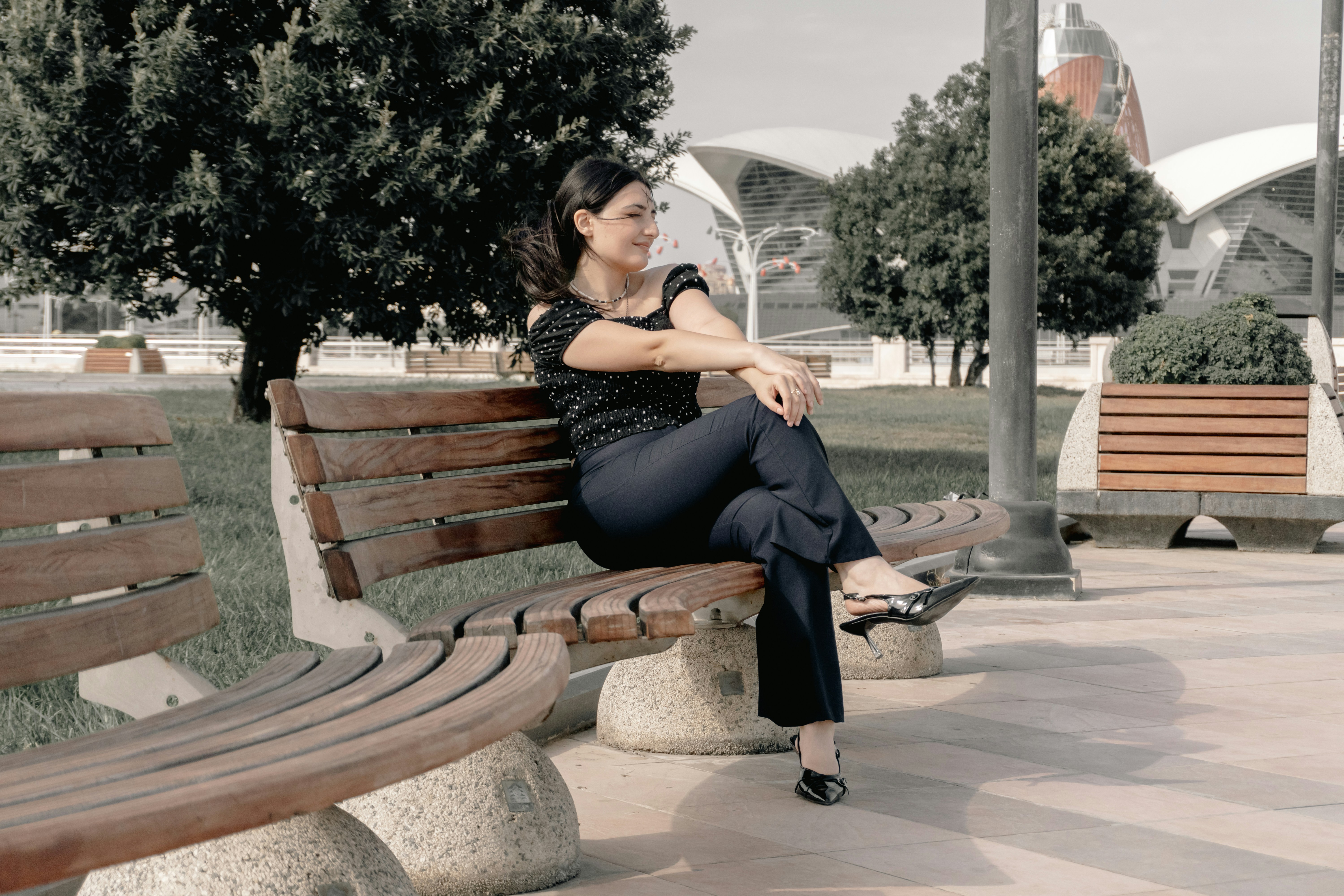 A woman in a polka dot top and dark trousers on a wooden bench
