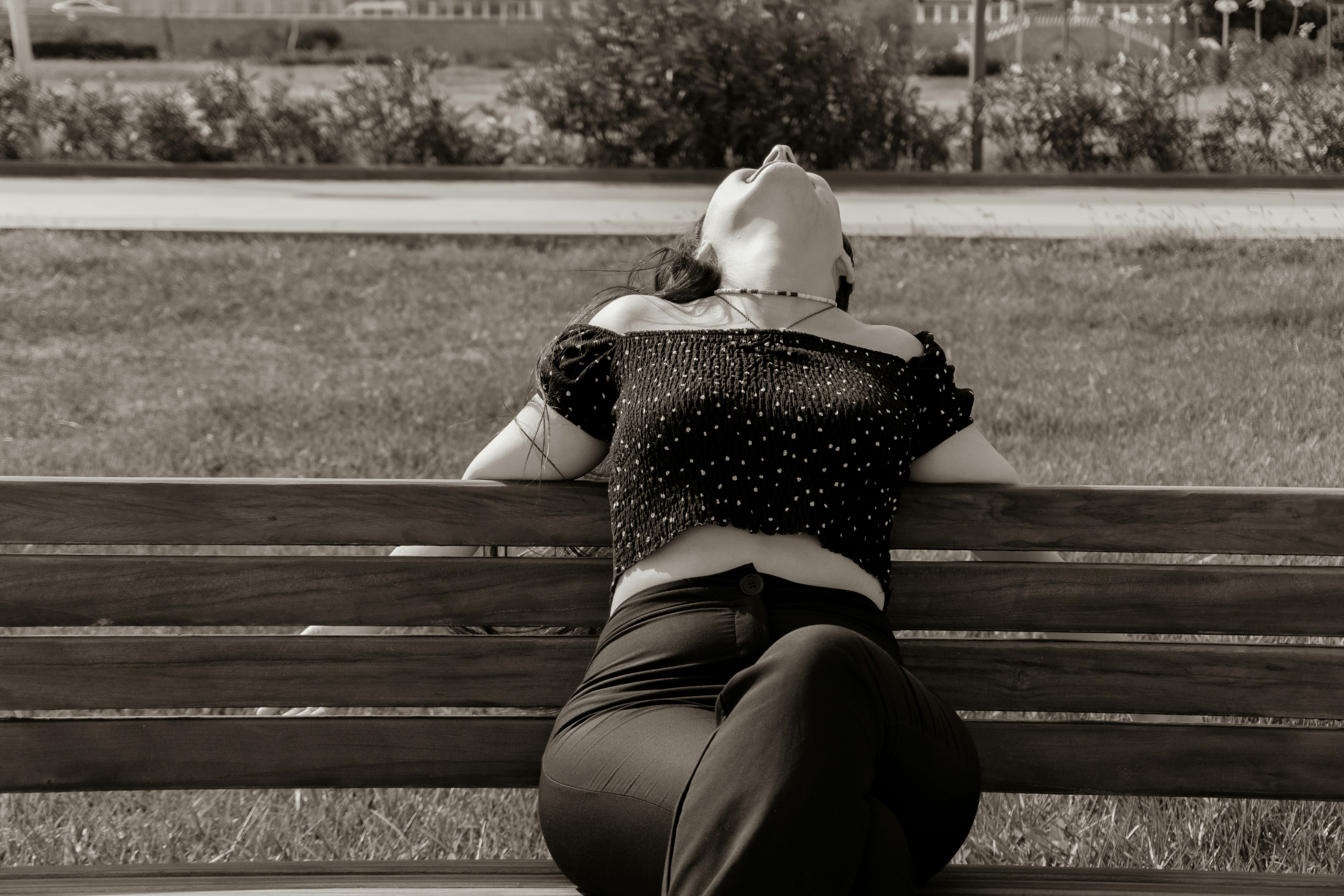 A woman in a black off-the-shoulder top leaning back on a wooden park bench