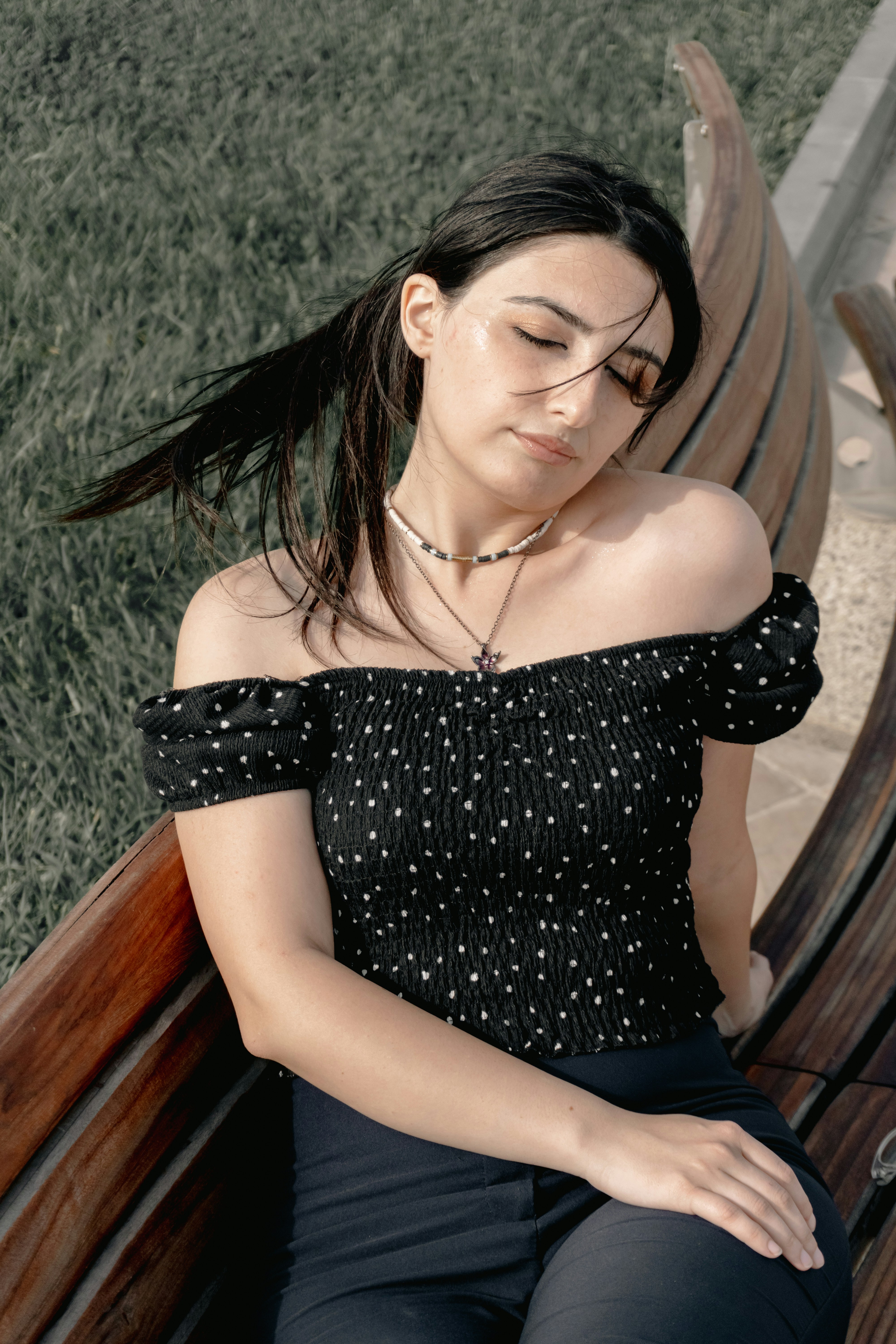 A woman with dark hair in a black polka dot top on a wooden bench
