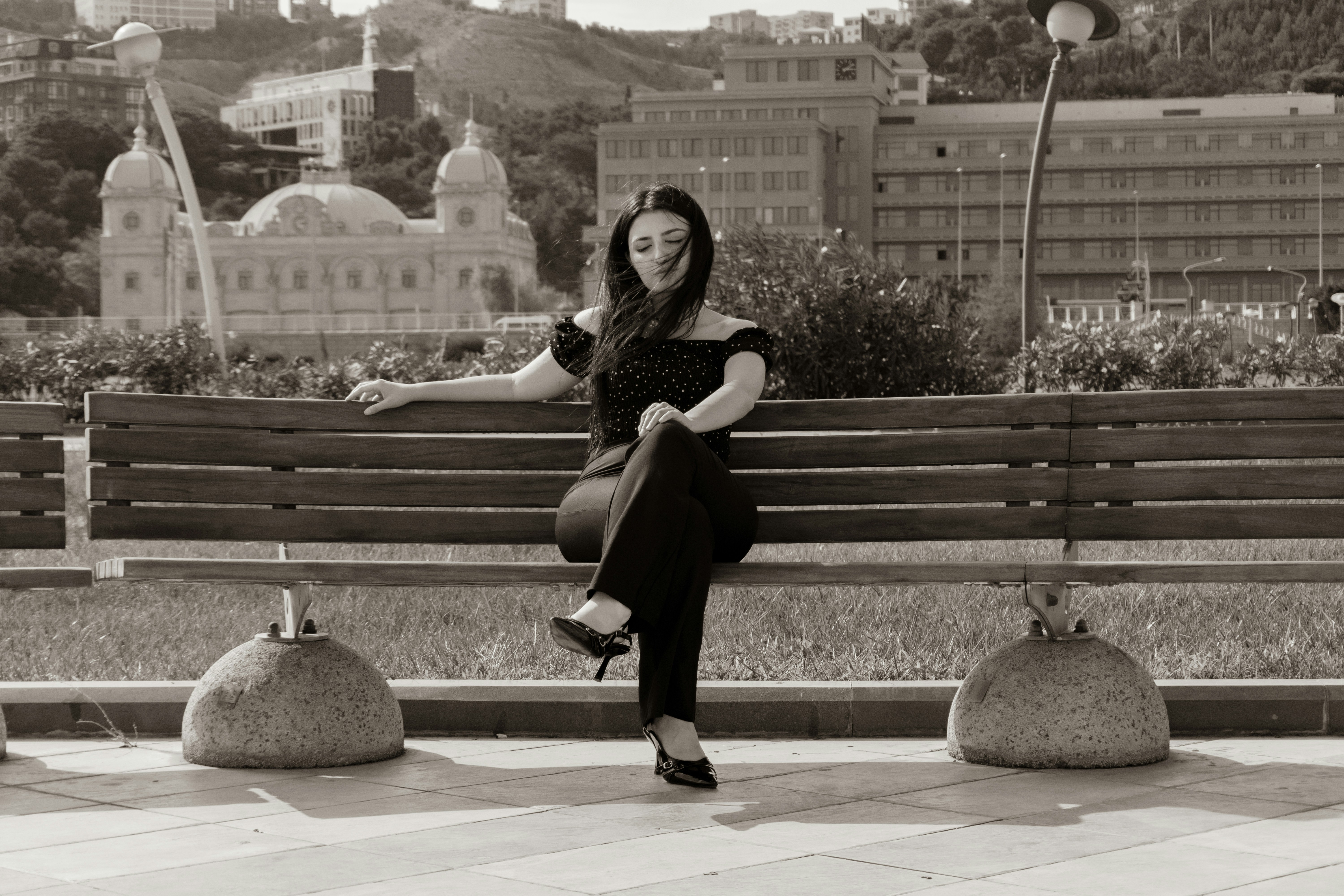 A woman in a polka dot top sitting on a wooden park bench