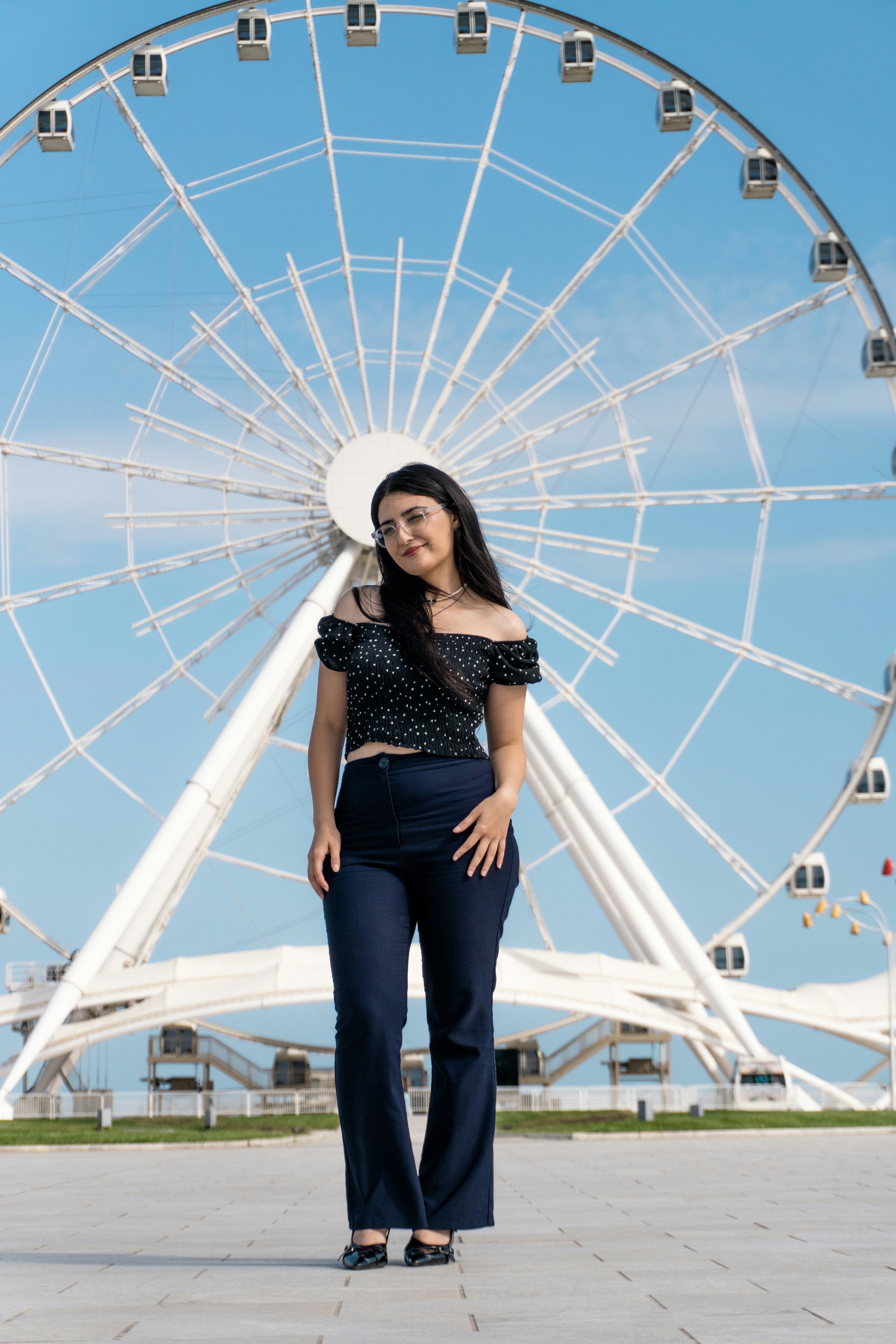 A woman in a black polka-dot top and navy trousers before a ferris wheel