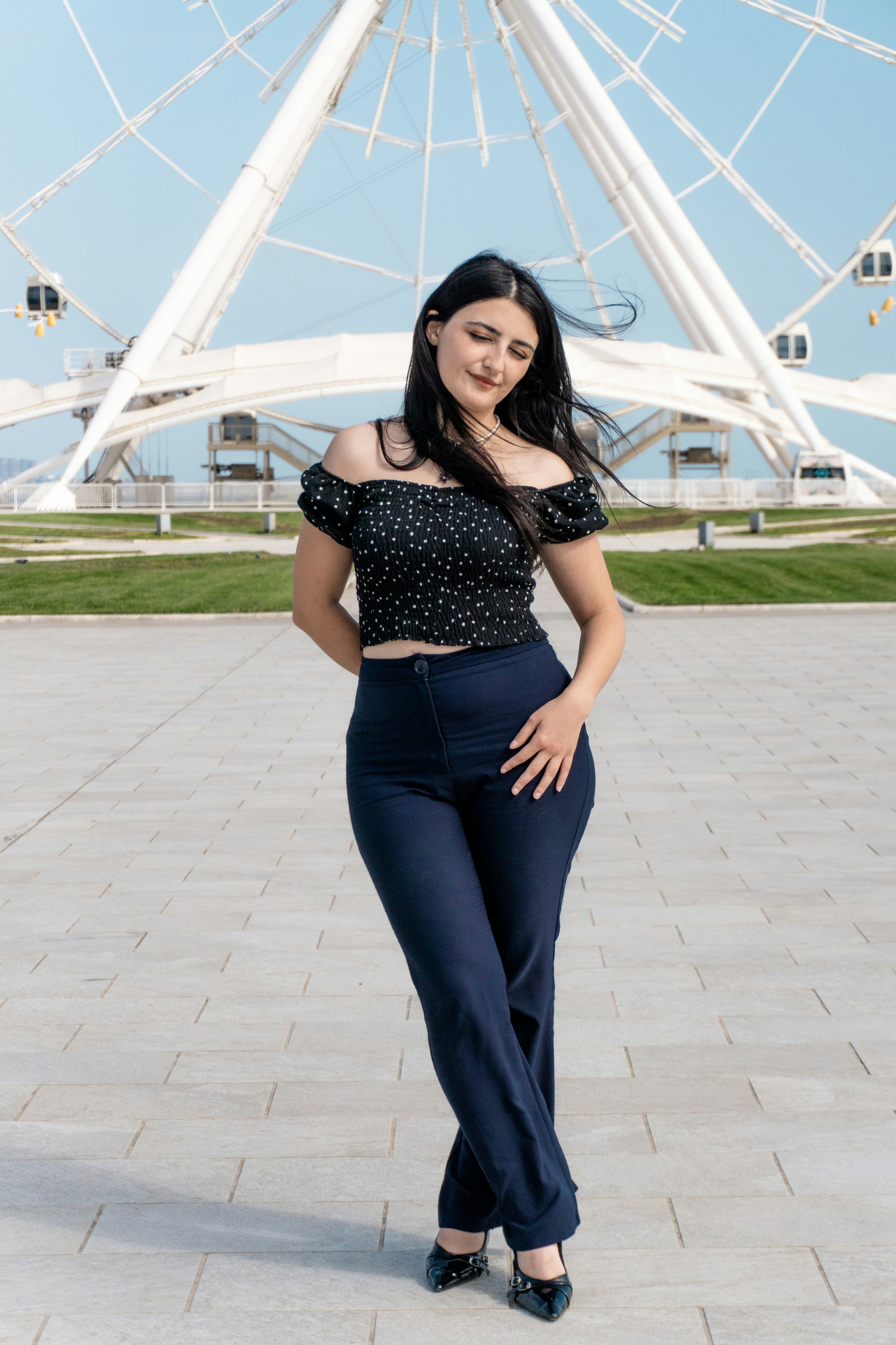 A woman in a black polka dot top and navy trousers before a ferris wheel