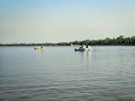 Two pedal boats with people on a calm lake near a tree-lined shore