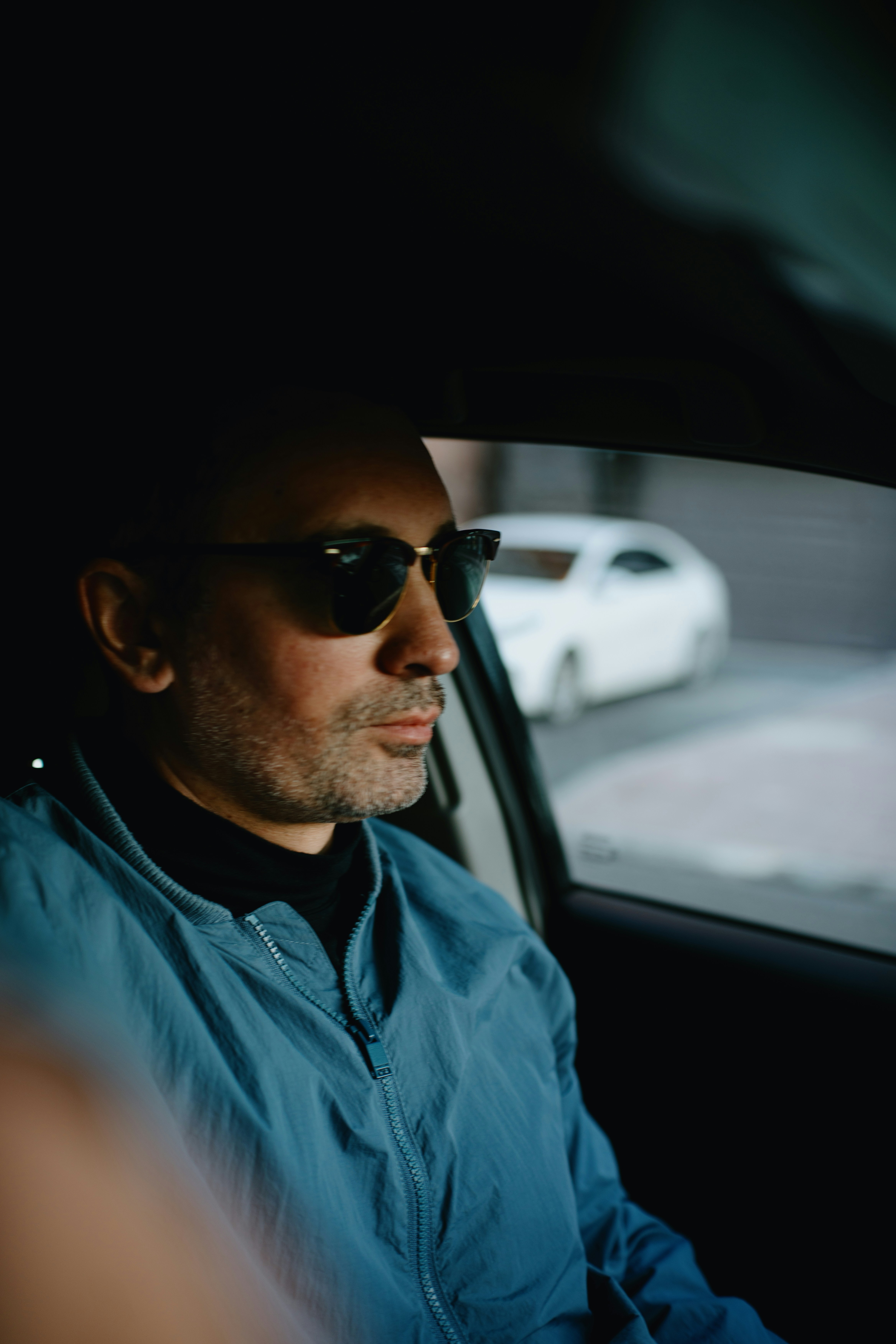 A man in sunglasses and a blue jacket driving a car